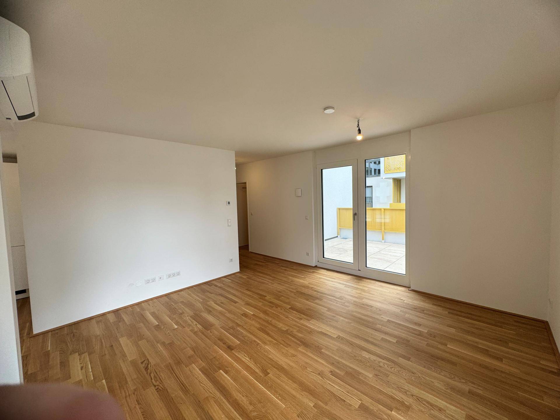 Heller Wohnbereich mit Parkettboden und Zugang zu einer großzügigen Außenterrasse.