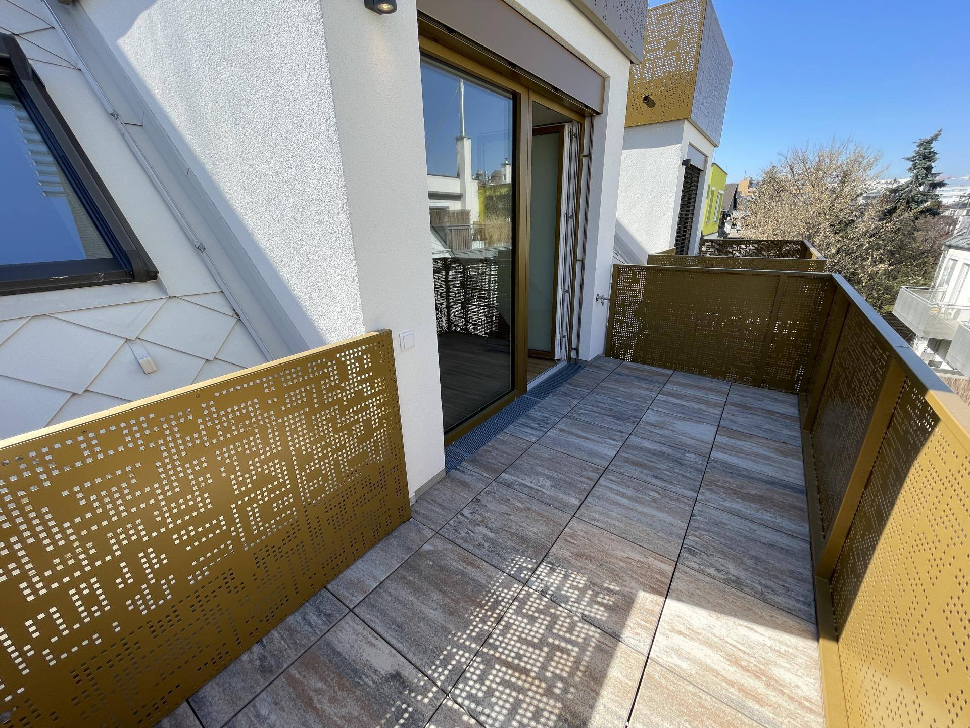 Heller Balkon mit modernen Fliesen und perforierten Metallgeländern, zugänglich durch eine Glasschiebetür.