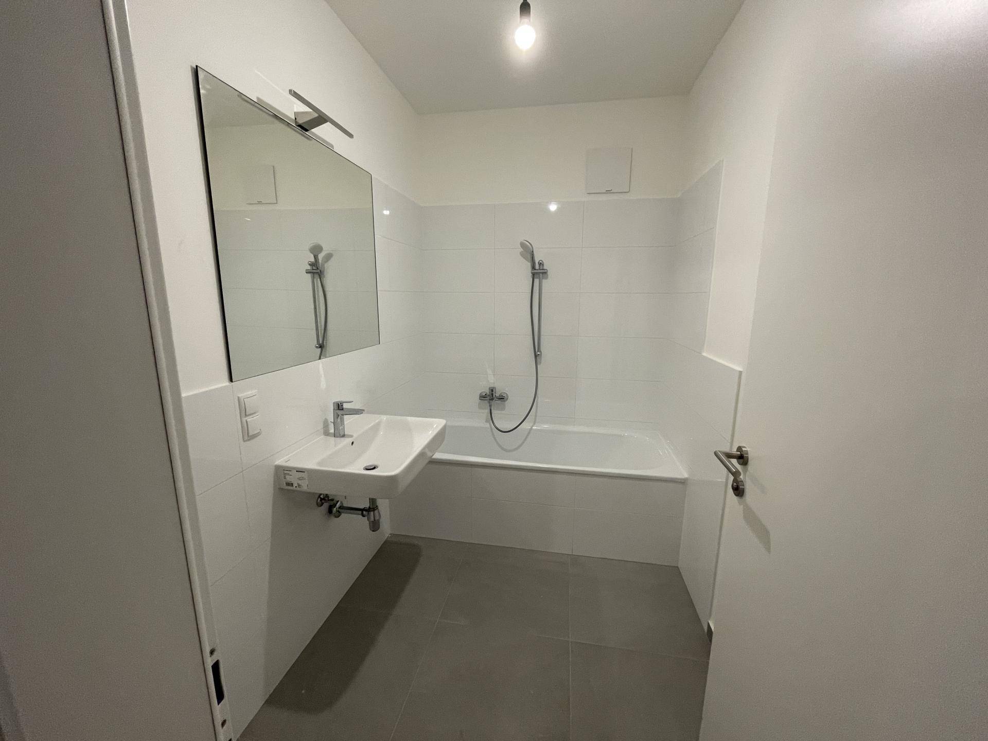 Modernes Badezimmer mit Badewanne, Waschbecken und weißen Fliesen, ausgestattet mit einem Spiegel.