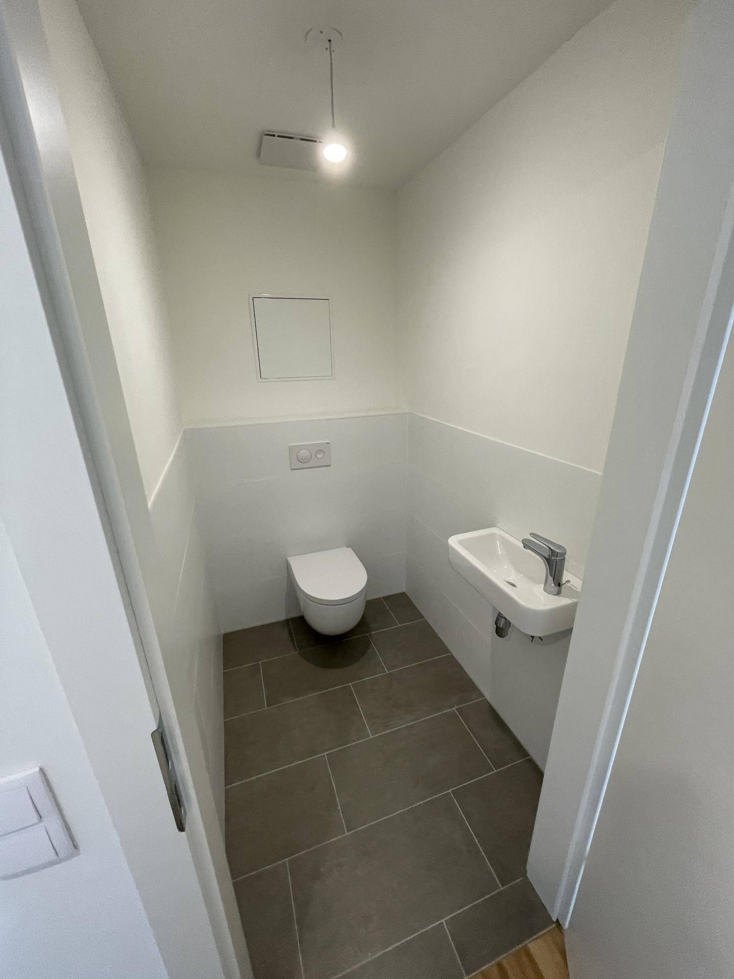 Separates Gäste-WC mit wandhängender Toilette und kleinem Waschbecken.