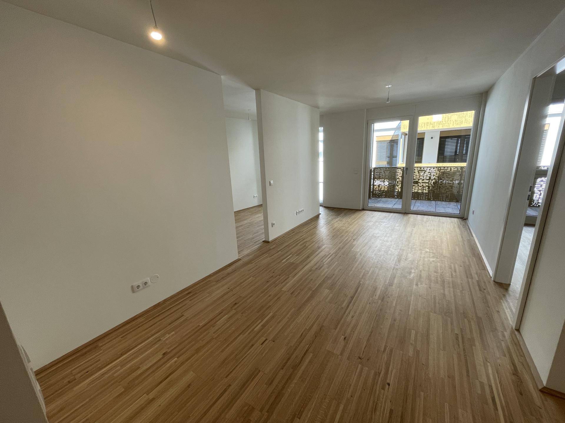 Geräumiger, heller Wohnbereich mit Eichenparkett und großen Fenstern zum Balkon.