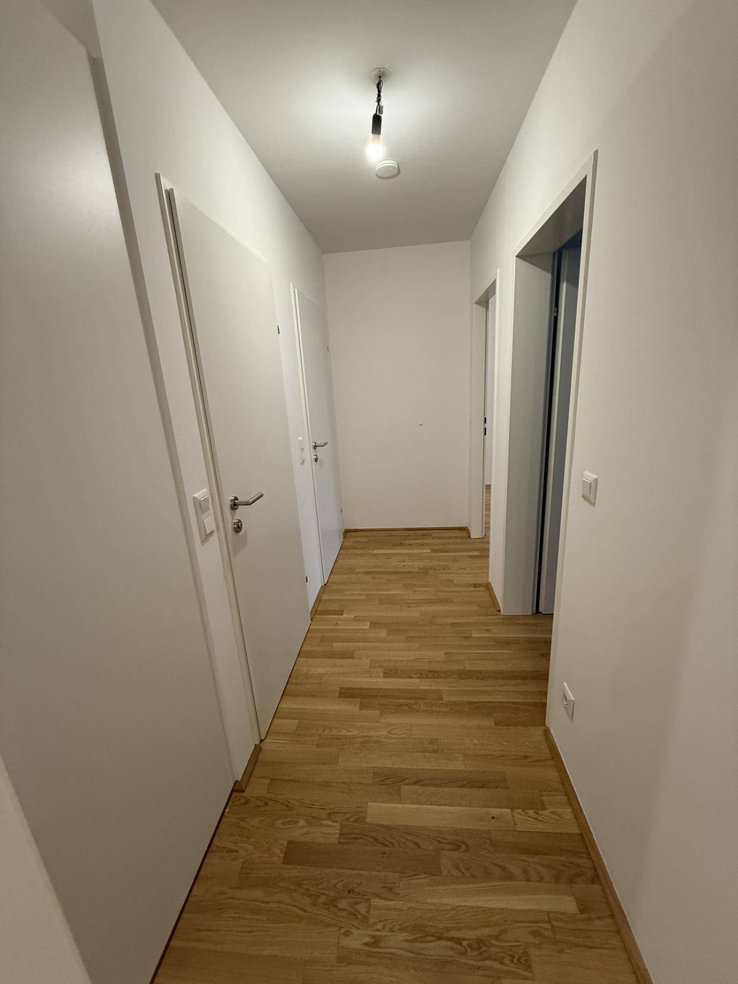 Heller Flur mit Parkettboden und weißen Türen, der zu den Zimmern führt.