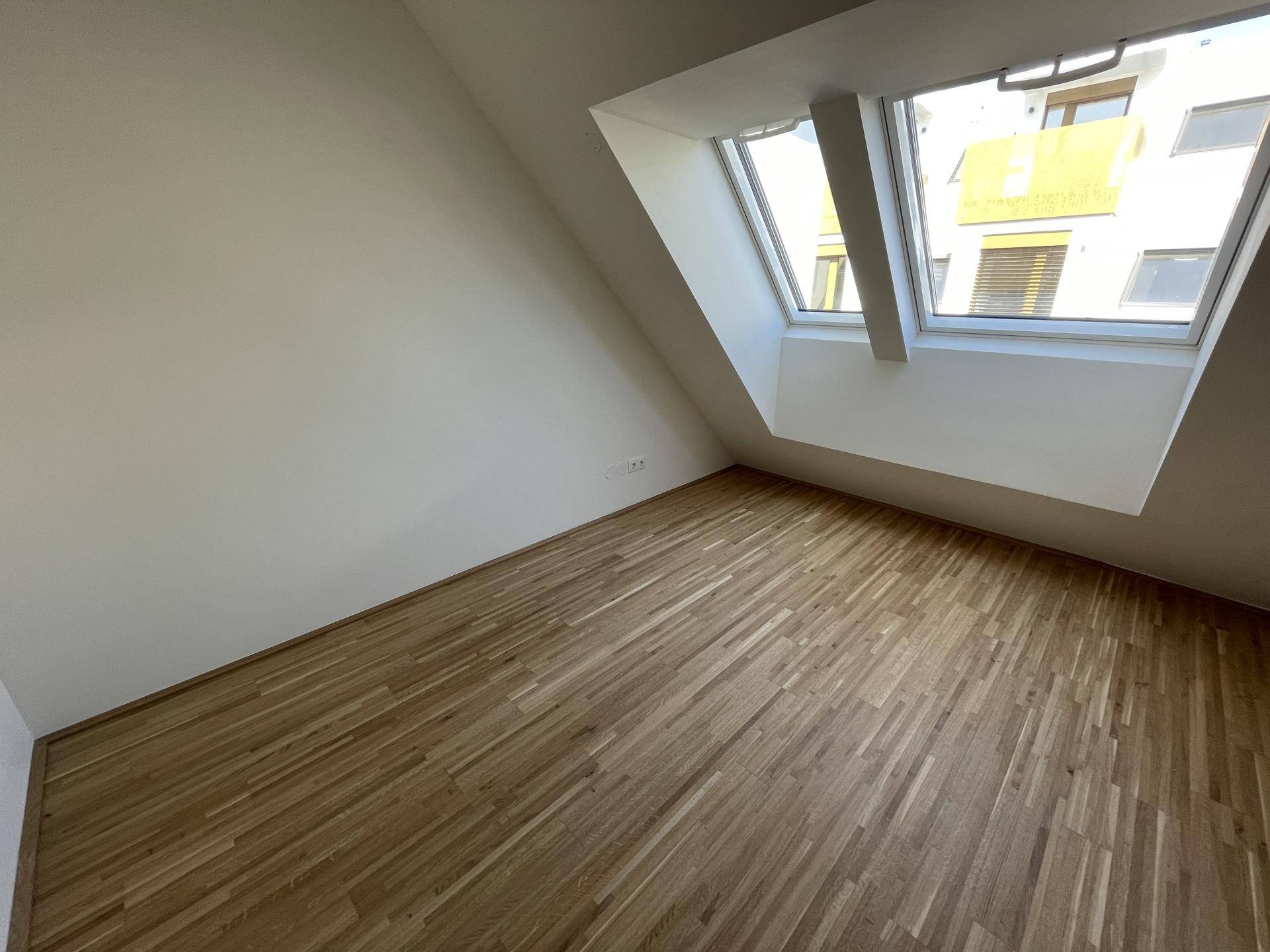 Heller Raum mit Holzboden und schrägen Wänden, beleuchtet durch ein großes Dachfenster.