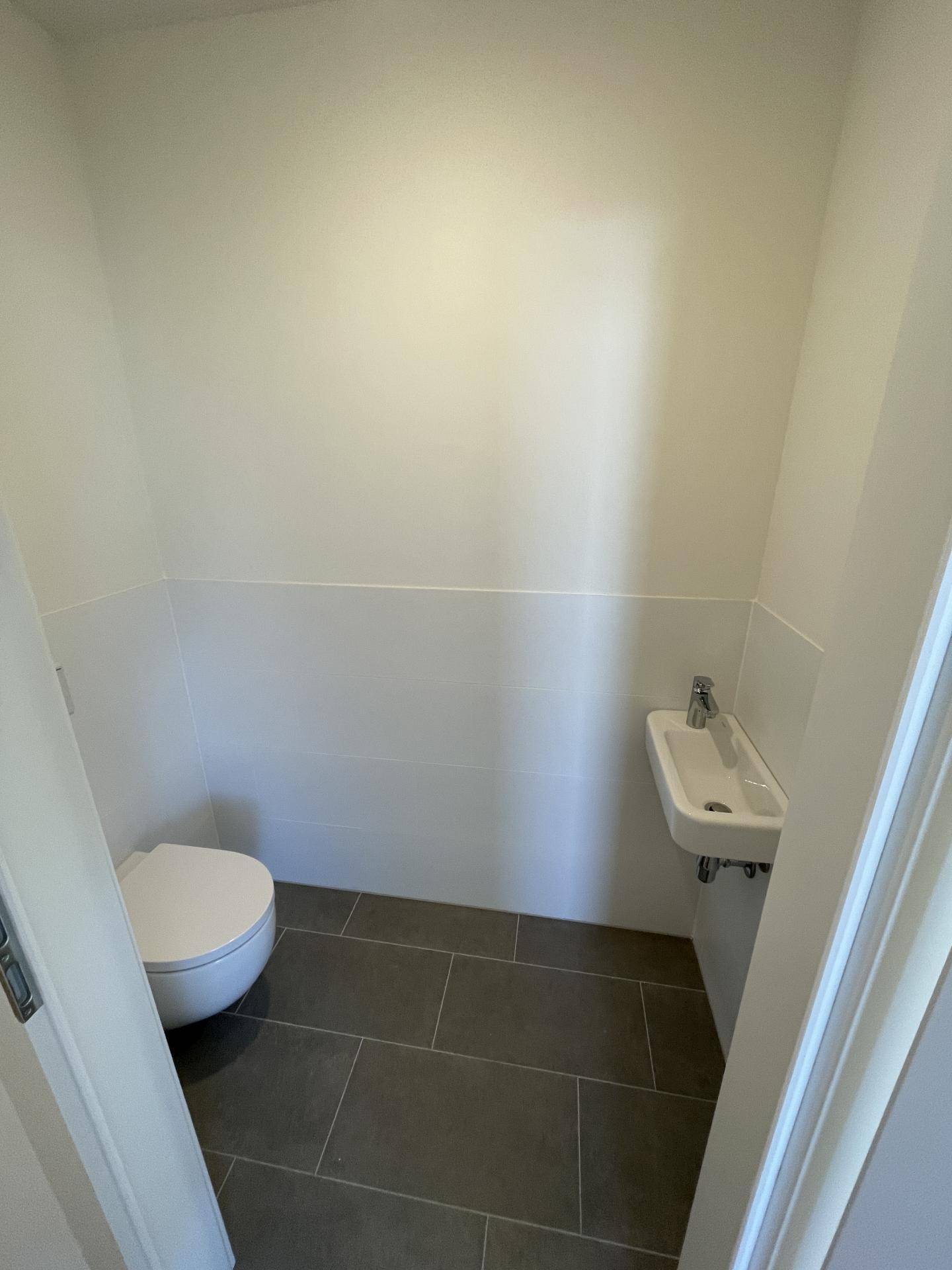 Separates Gäste-WC mit wandhängender Toilette, kleinem Waschbecken und grauen Fliesen.