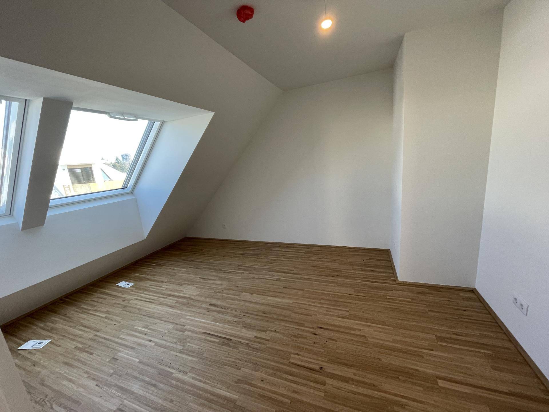 Helles Zimmer mit Parkettboden, Dachfenstern und schrägen Wänden im Dachgeschoss.
