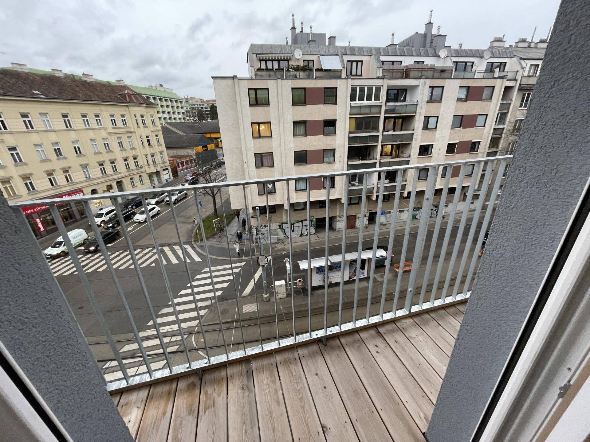 Balkon mit Holzboden und Metallgeländer bietet einen Blick auf die belebte Stadtstraße und umliegende Gebäude.