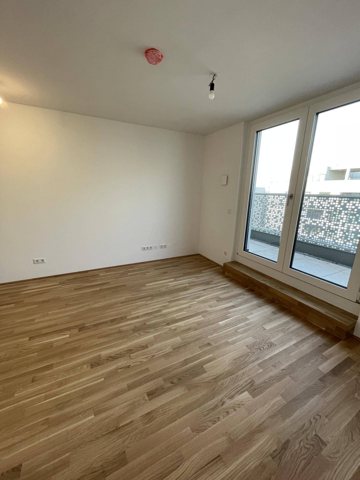 Heller Raum mit Eichenparkett und großen Fenstertüren, die Zugang zu einem Außenbereich bieten.