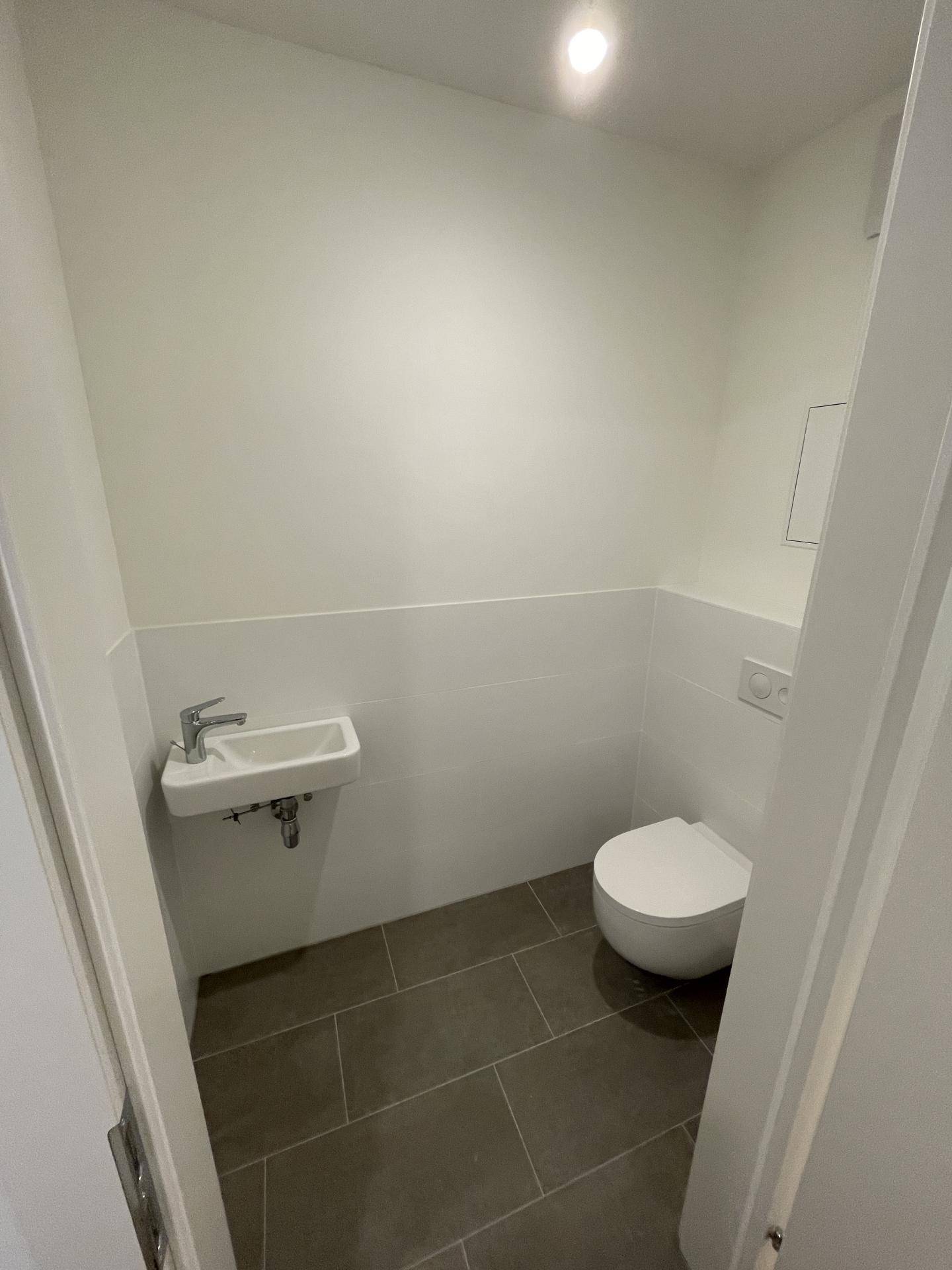Modernes Gäste-WC mit dunklem Fliesenboden, wandhängendem WC und kleinem Handwaschbecken.