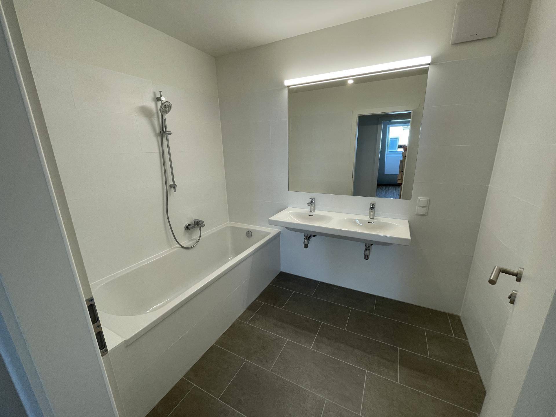 Modernes Badezimmer mit Badewanne, Doppelwaschbecken und großem Spiegel.