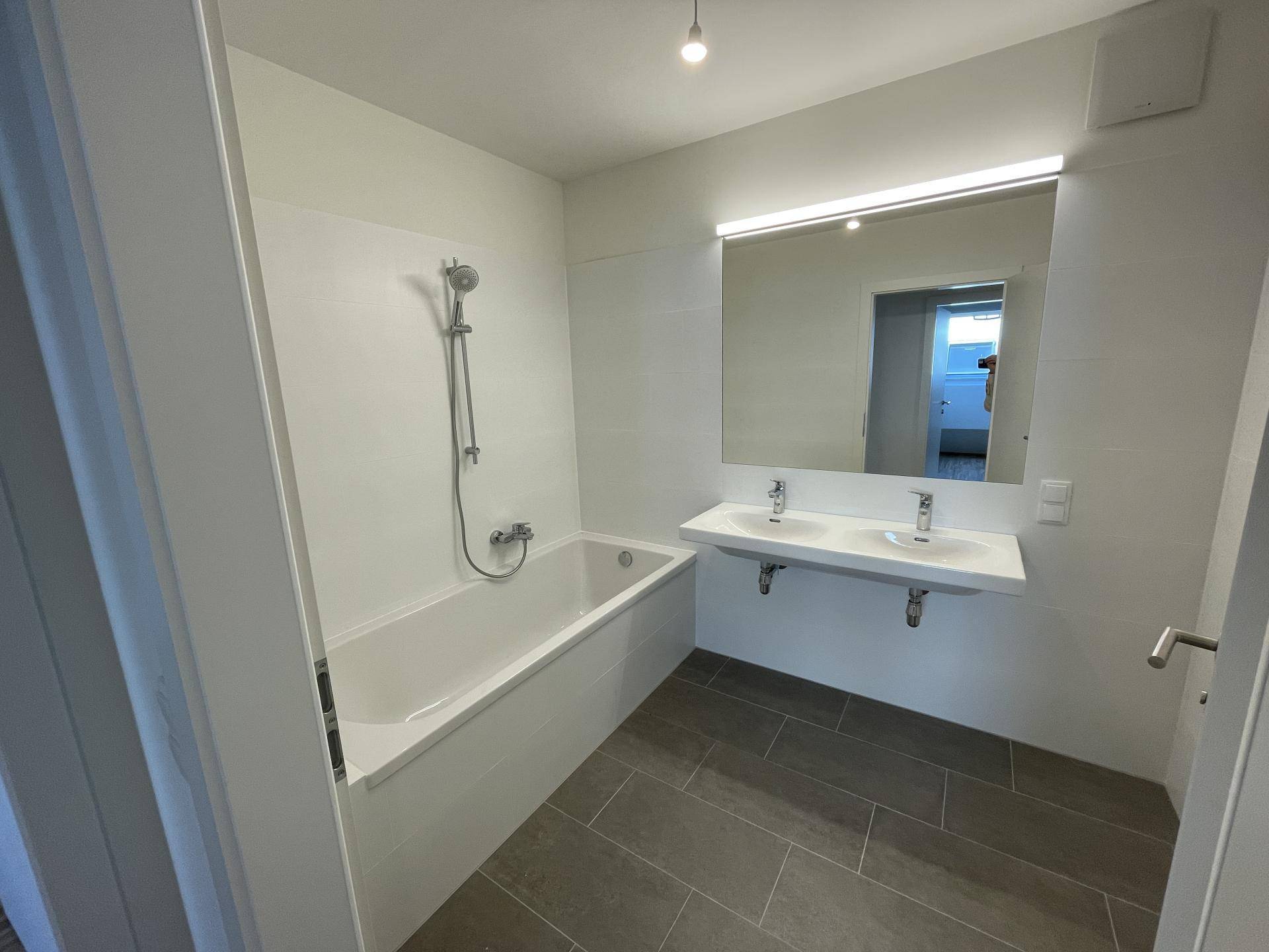 Modernes Badezimmer mit Badewanne, Doppelwaschbecken und großem Spiegel, in hellen Tönen.