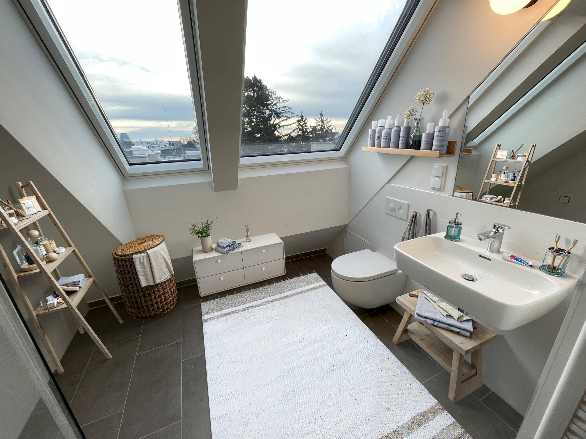 Helles Badezimmer im Dachgeschoss mit modernen Fliesen, wandhängendem WC und großen Dachfenstern.