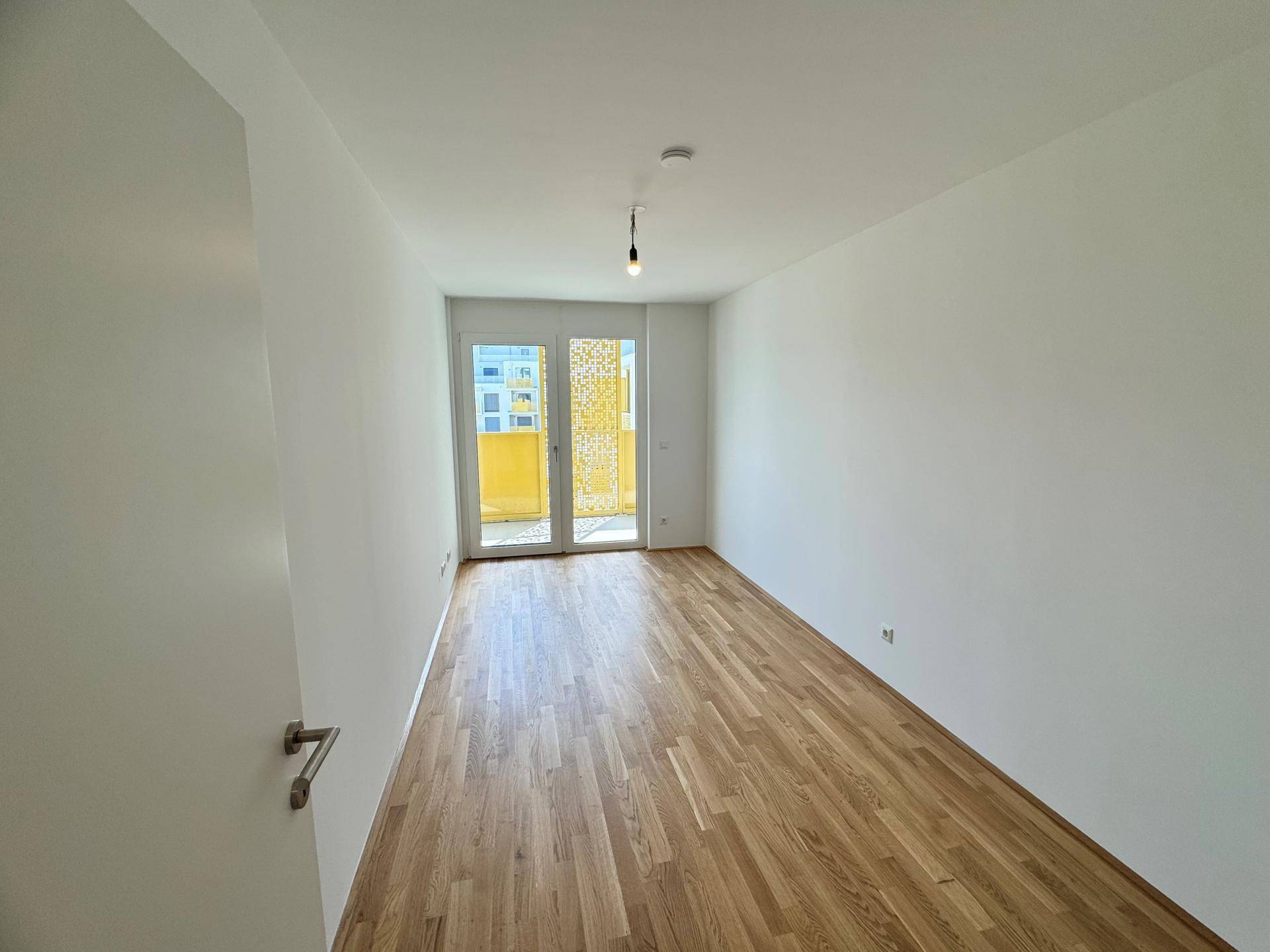 Helles, unmöbliertes Zimmer mit Parkettboden und direktem Balkonzugang.