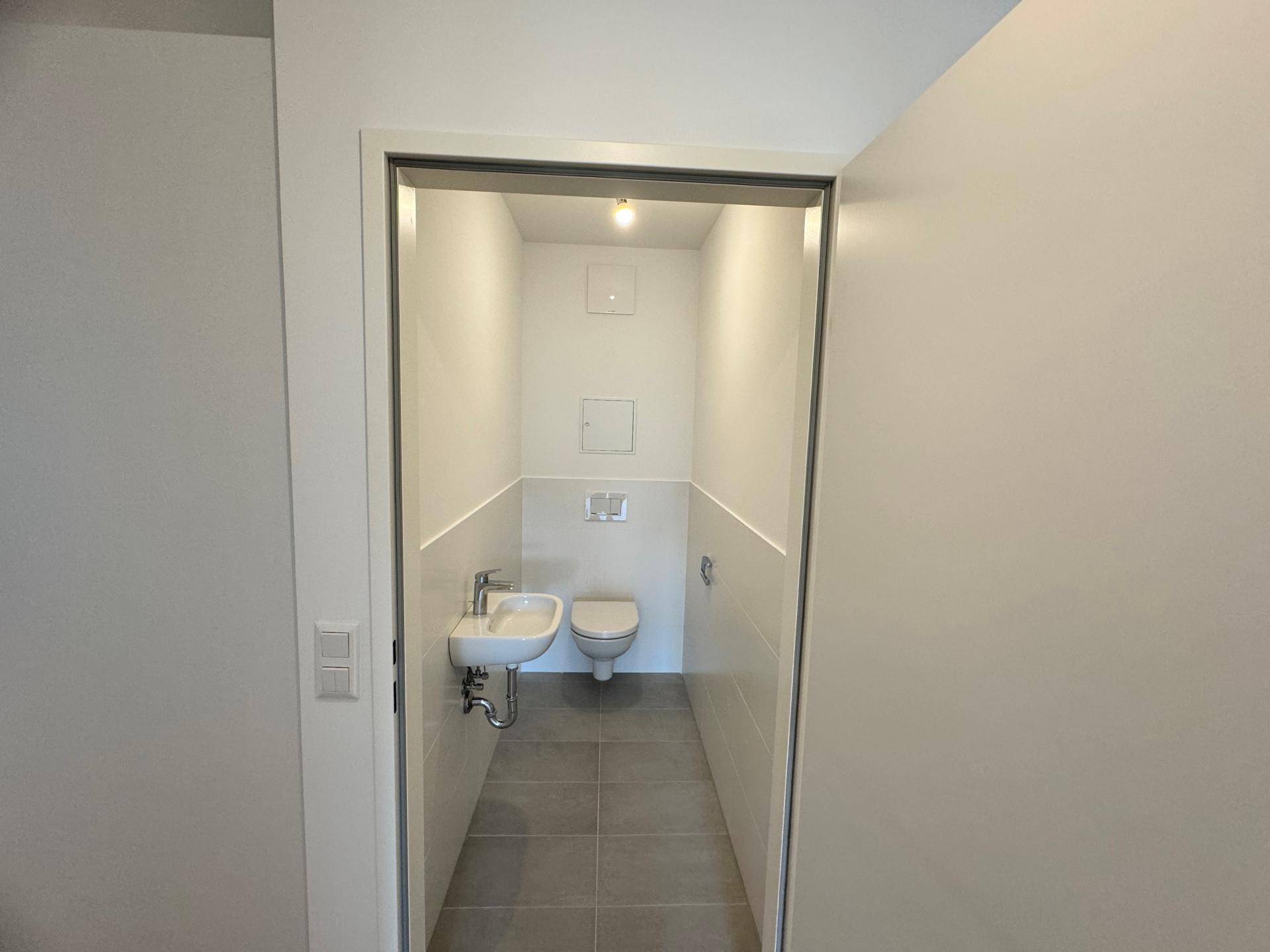Modernes Gäste-WC mit Wand-WC, kleinem Waschbecken und Fliesenboden.