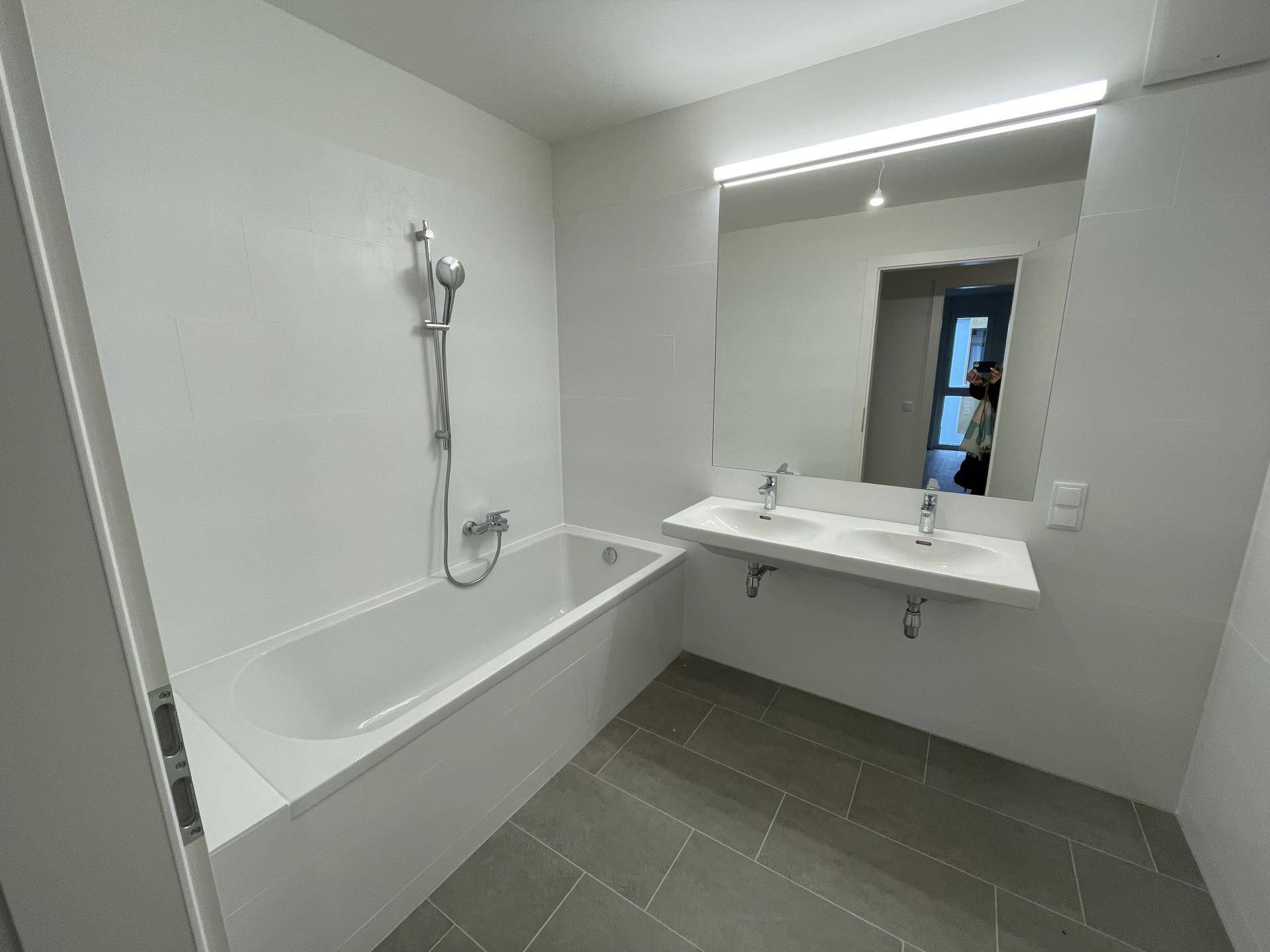Modernes Badezimmer mit Badewanne, Doppelwaschbecken und hellgrauen Fliesen.