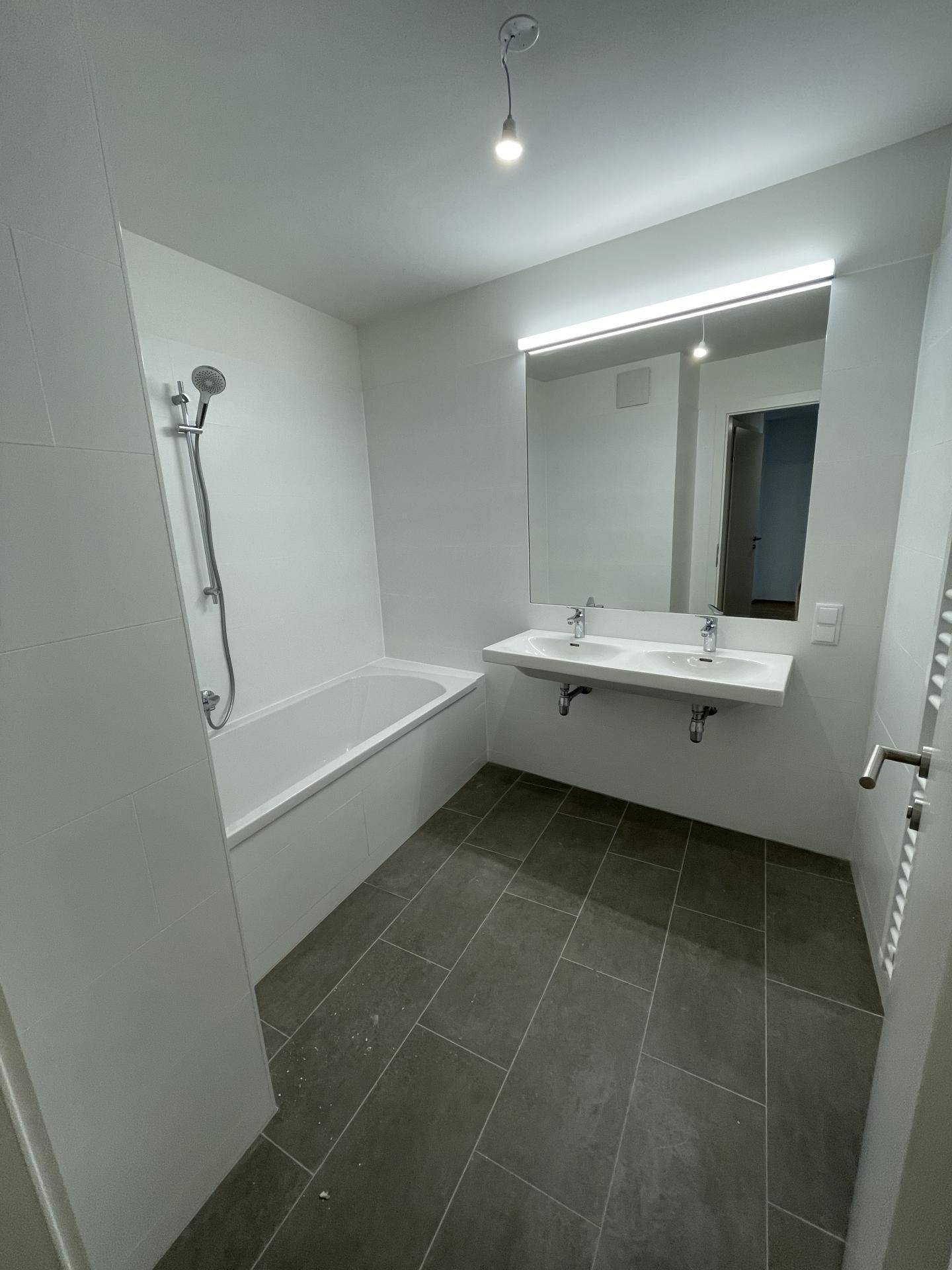 Modernes Badezimmer mit dunklen Fliesen, Badewanne mit Duschfunktion und Doppelwaschbecken.