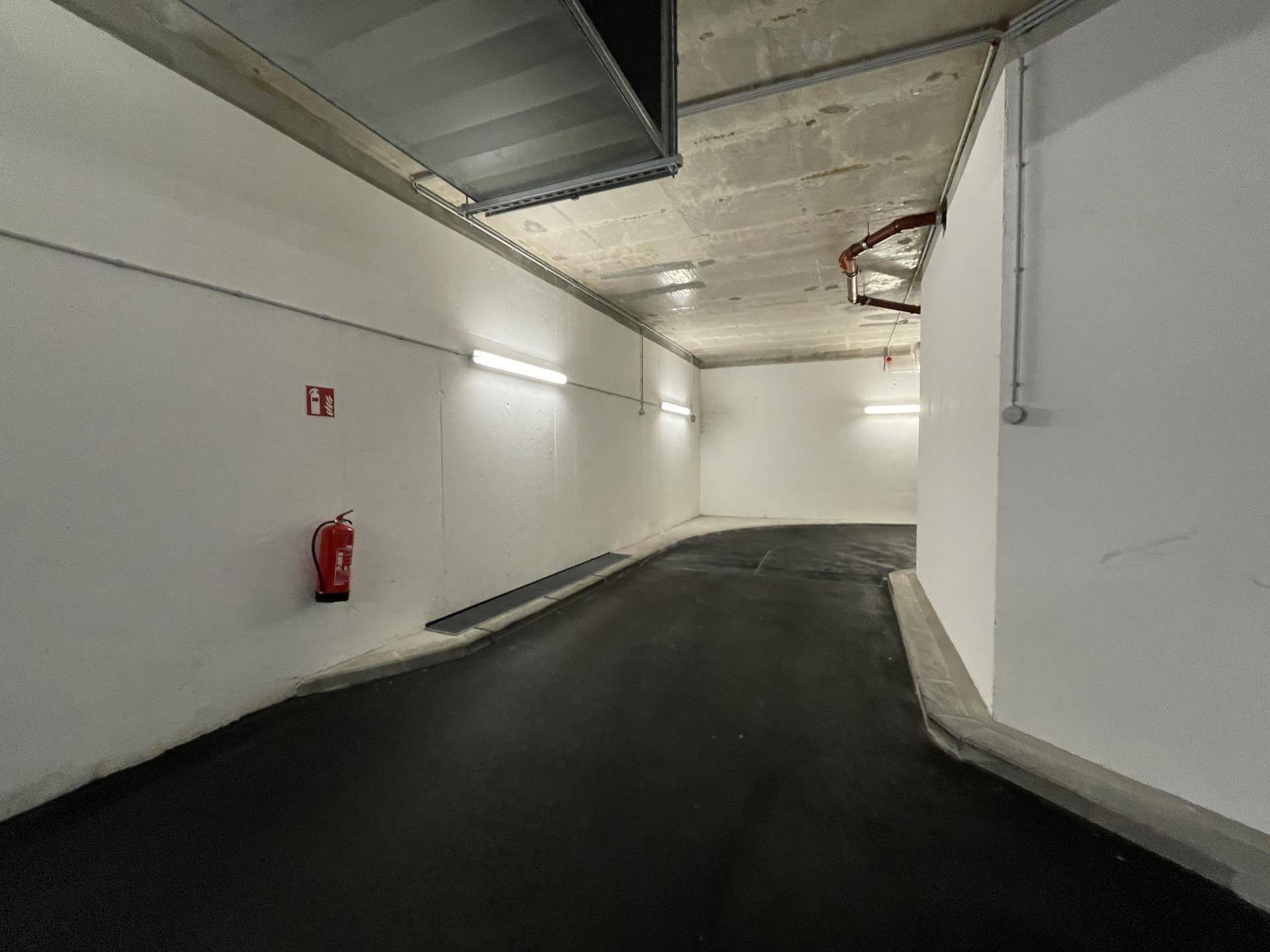 Zufahrtsrampe zur Tiefgarage mit hellen Wänden, guter Beleuchtung und Brandschutzvorrichtungen.