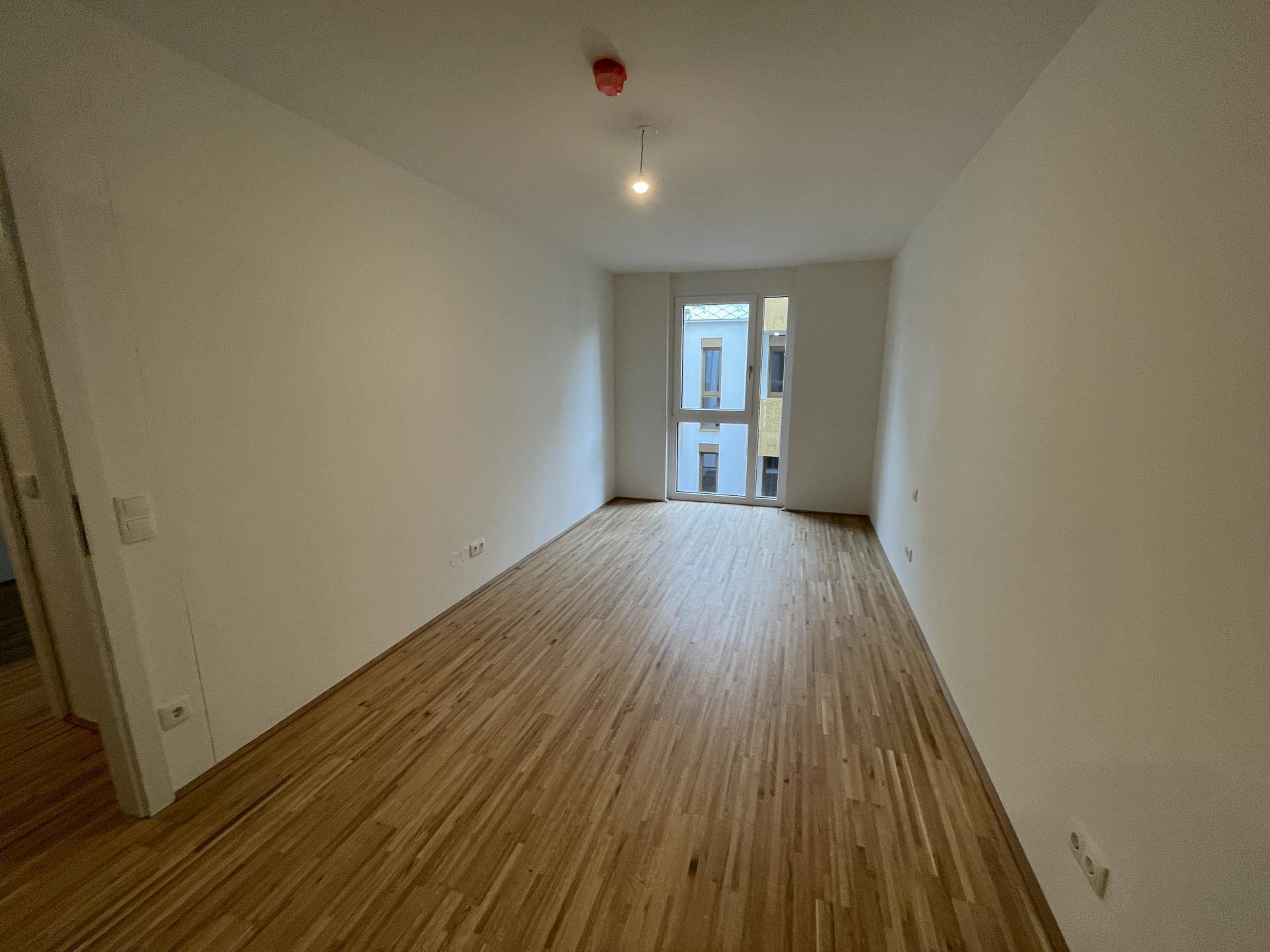 Helles, leeres Schlafzimmer mit Parkettboden und einem großen Fenster.