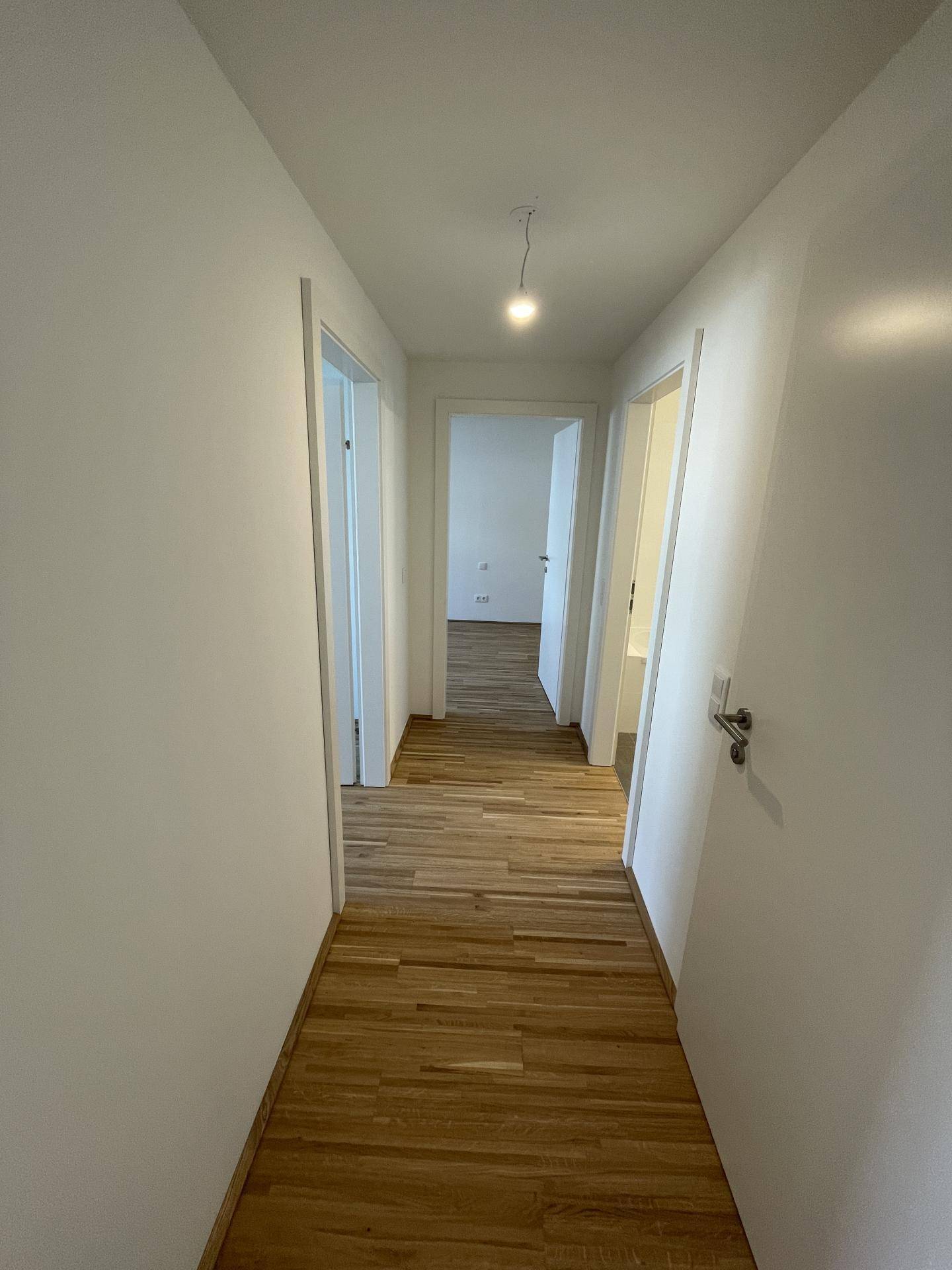 Heller Flur mit Holzboden, der zu verschiedenen Räumen der Wohnung führt.