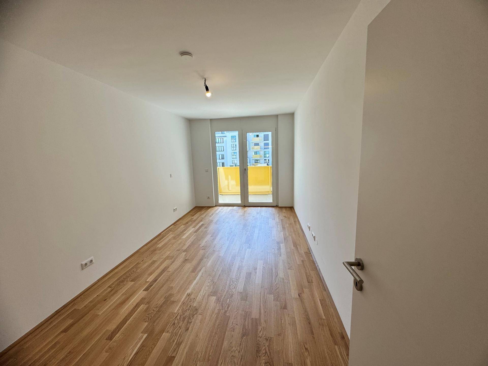 Leeres Schlafzimmer mit Parkettboden und Zugang zu einem Balkon.