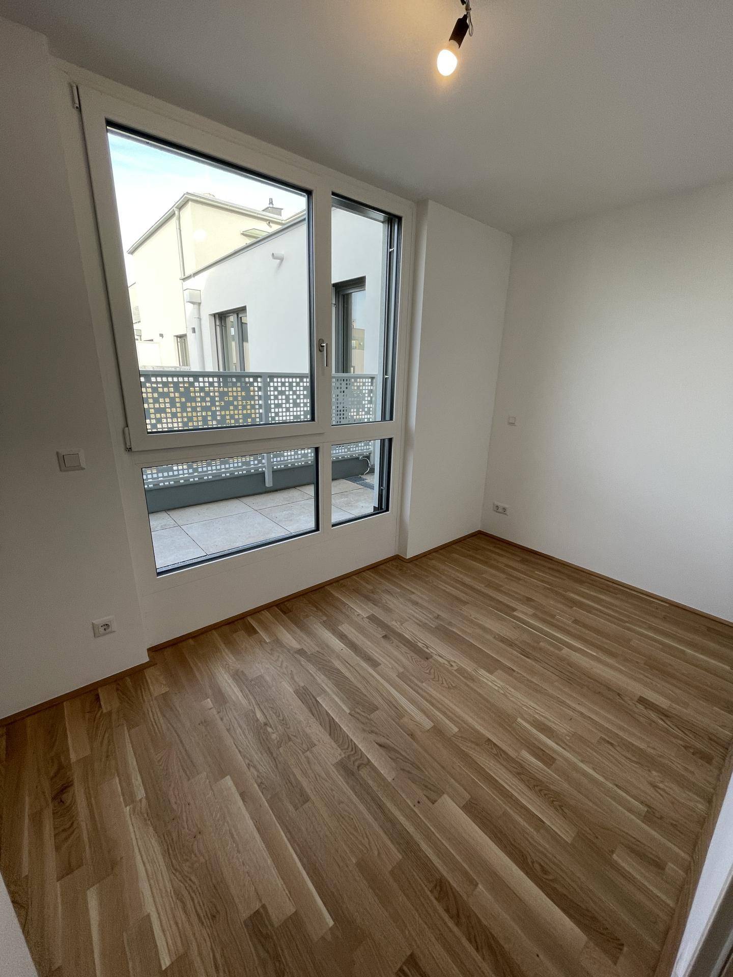 Geräumiges Zimmer mit Holzparkett und großen Fenstern, die viel Tageslicht hereinlassen.