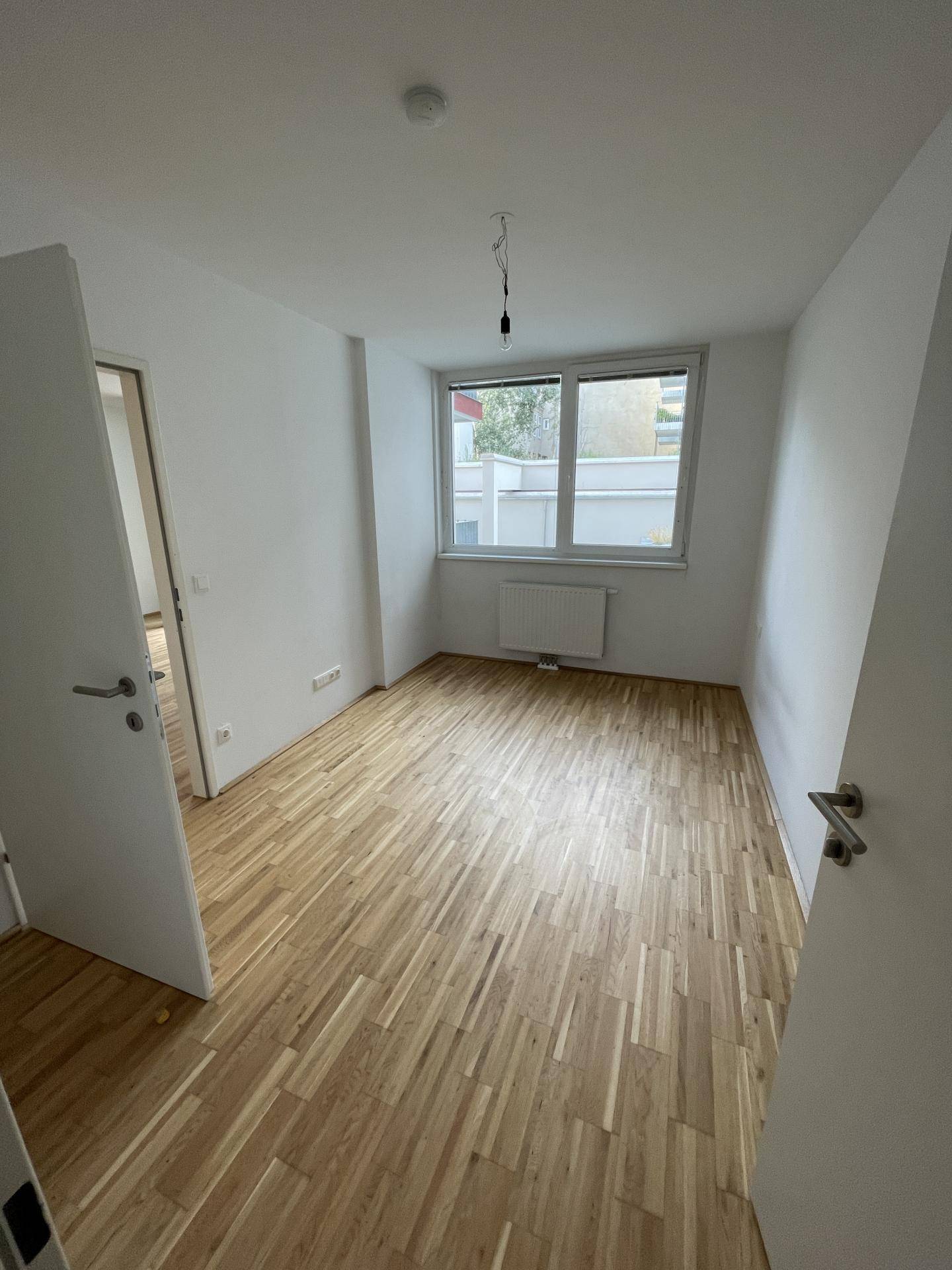 Helles Schlafzimmer mit Parkettboden und einem großen Fenster, das viel Tageslicht hereinlässt.