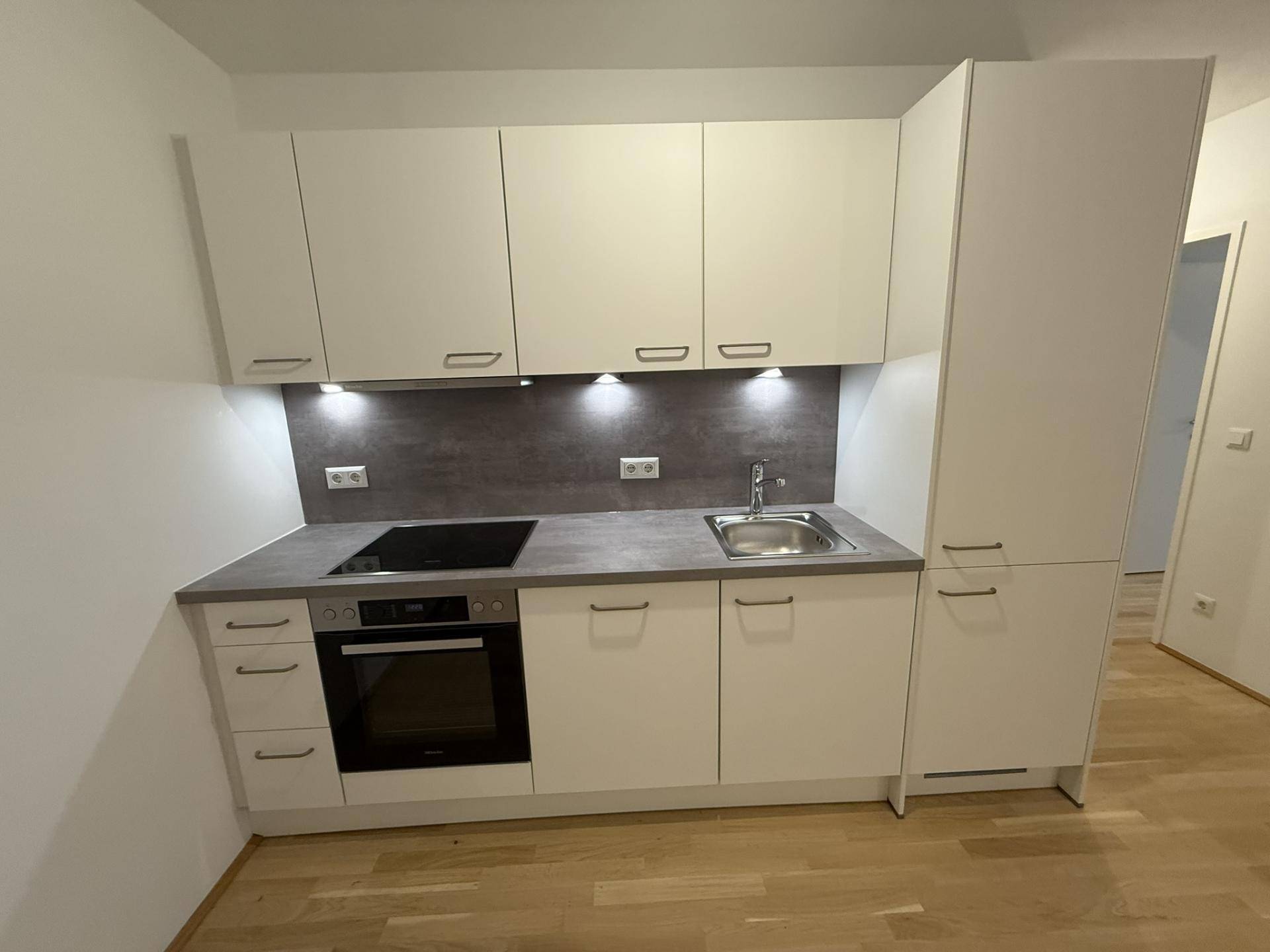 Moderne Einbauküche mit weißen Schränken, Induktionskochfeld und integriertem Backofen.