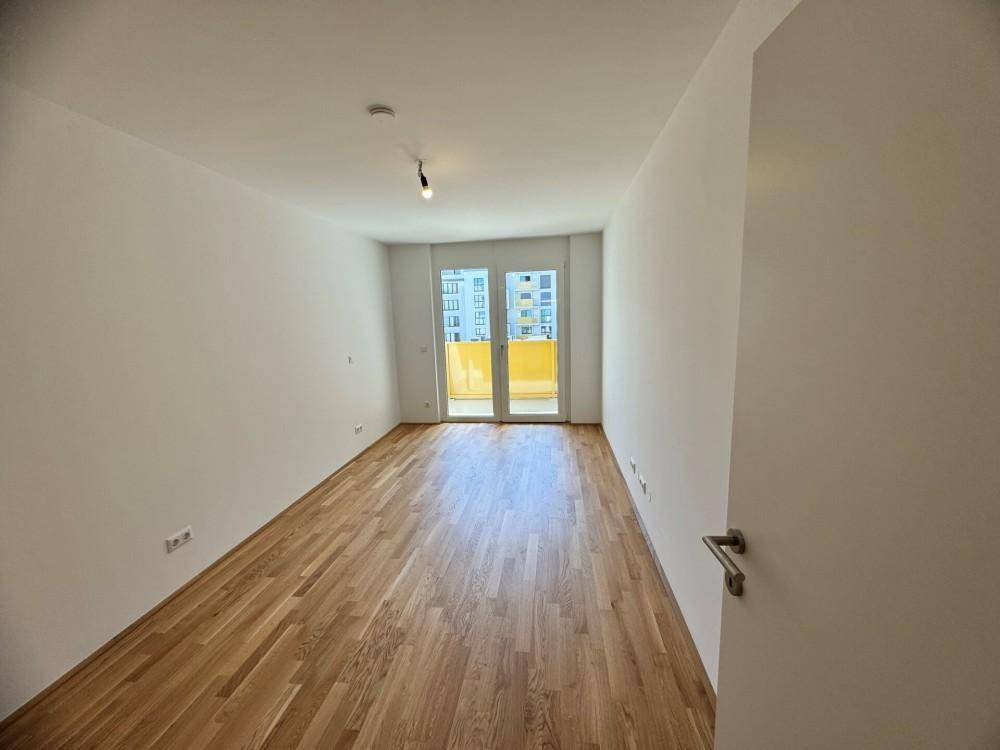 Helles Schlafzimmer mit Holzboden und Zugang zu einem Balkon, unmöbliert und geräumig.