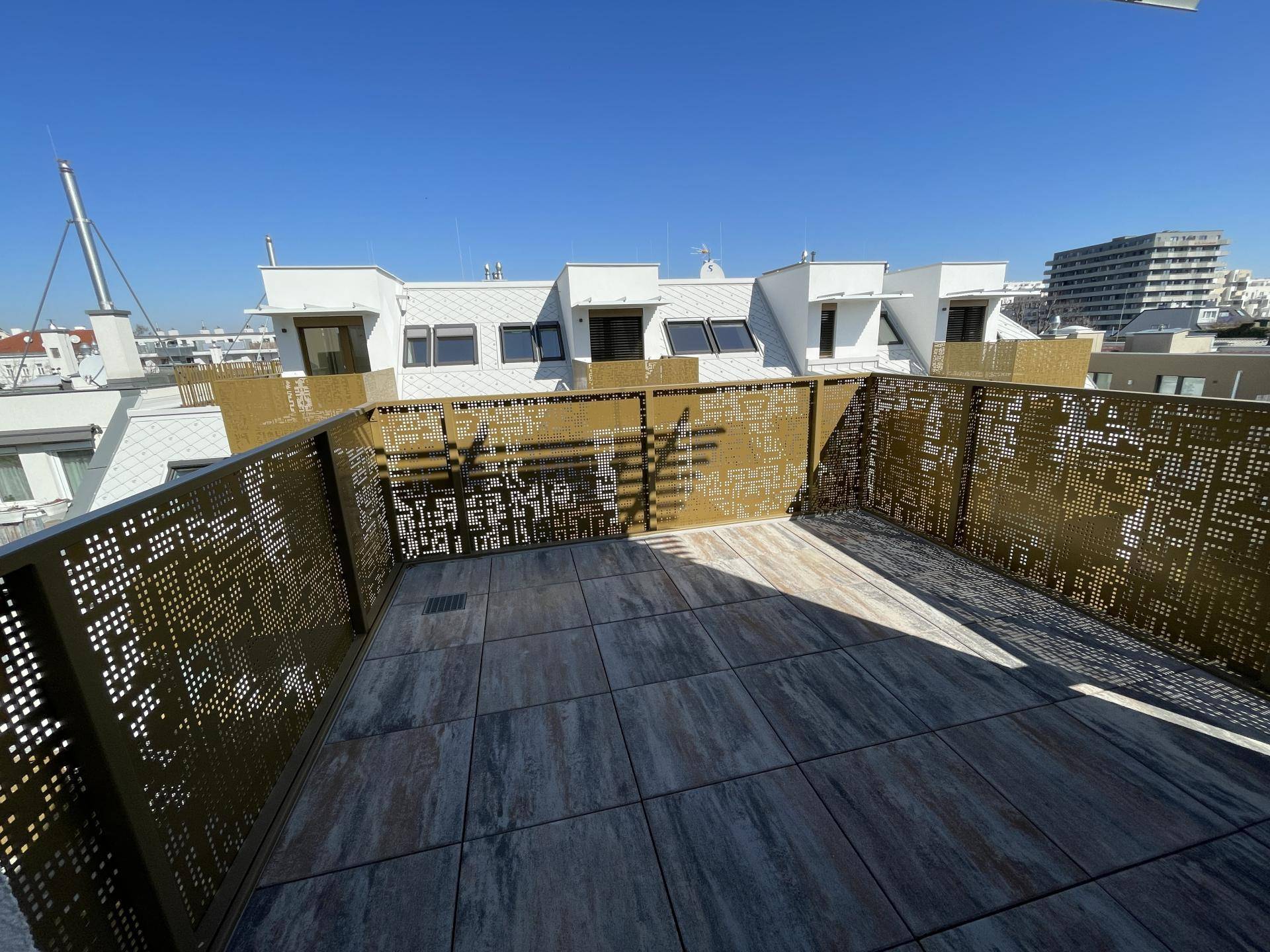 Geräumige Dachterrasse mit modernen Fliesen und dekorativer Metallbrüstung unter blauem Himmel.