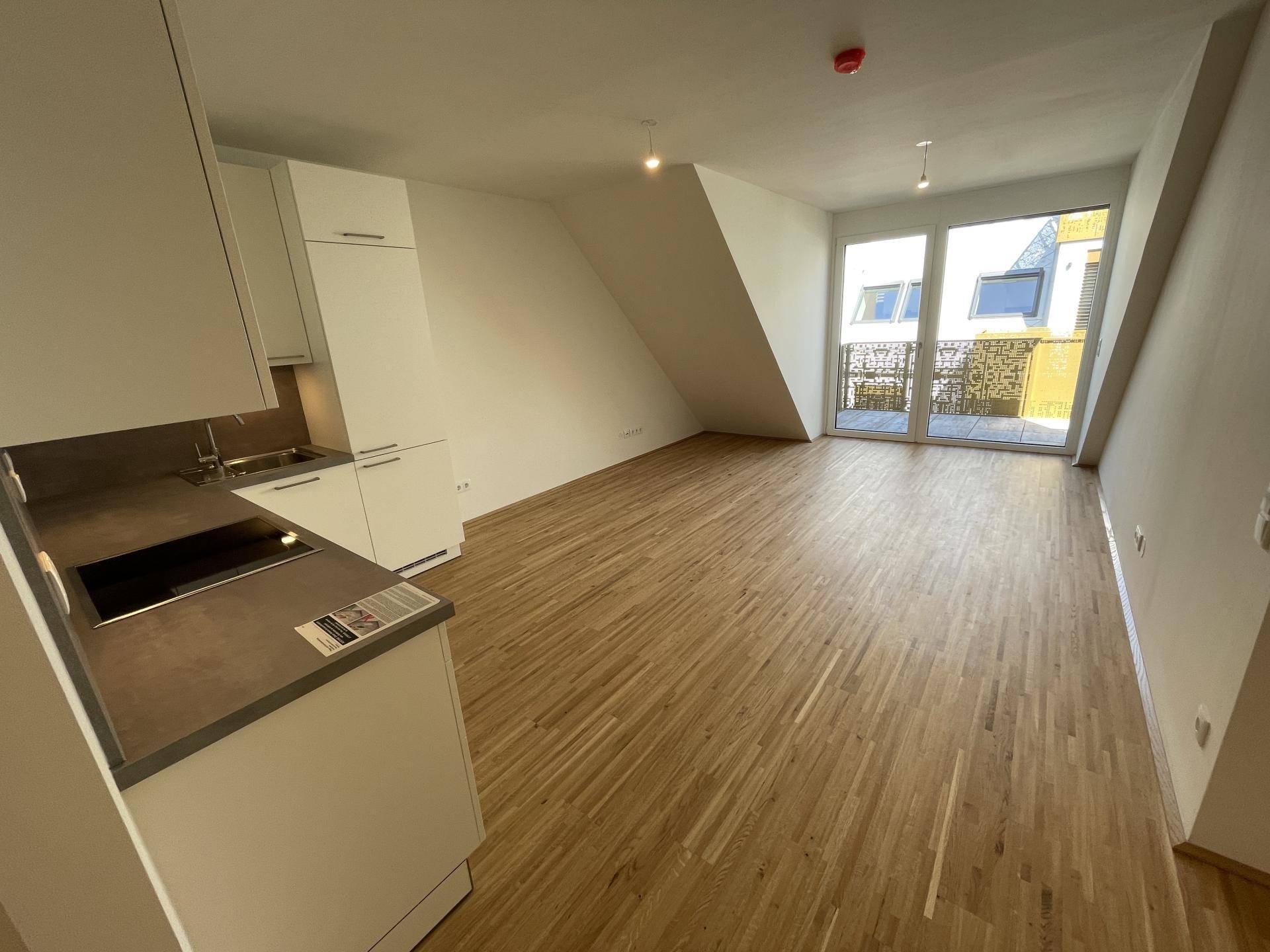 Heller offener Wohnbereich mit Holzboden, großen Fenstern und Zugang zum Balkon.