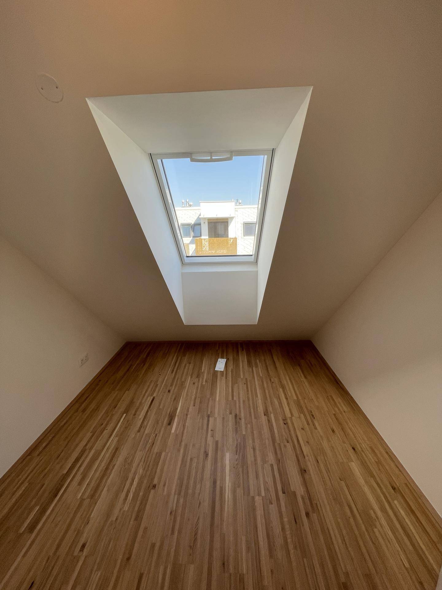 Dachgeschosszimmer mit Parkettboden und einem großen Dachfenster, das viel Licht hereinlässt.