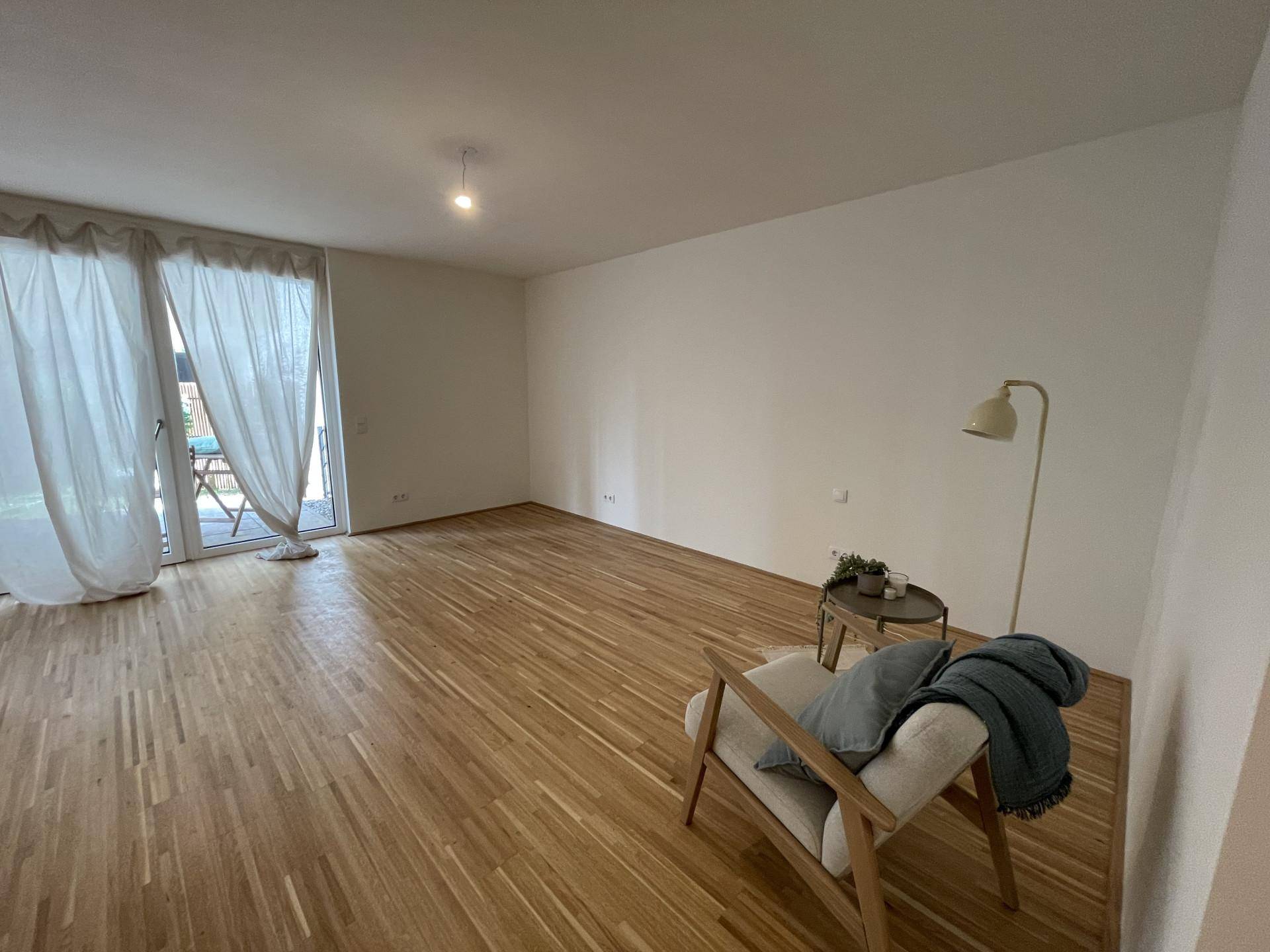 Geräumiger Wohnbereich mit Holzboden, großen Fenstern und Zugang zur Terrasse.