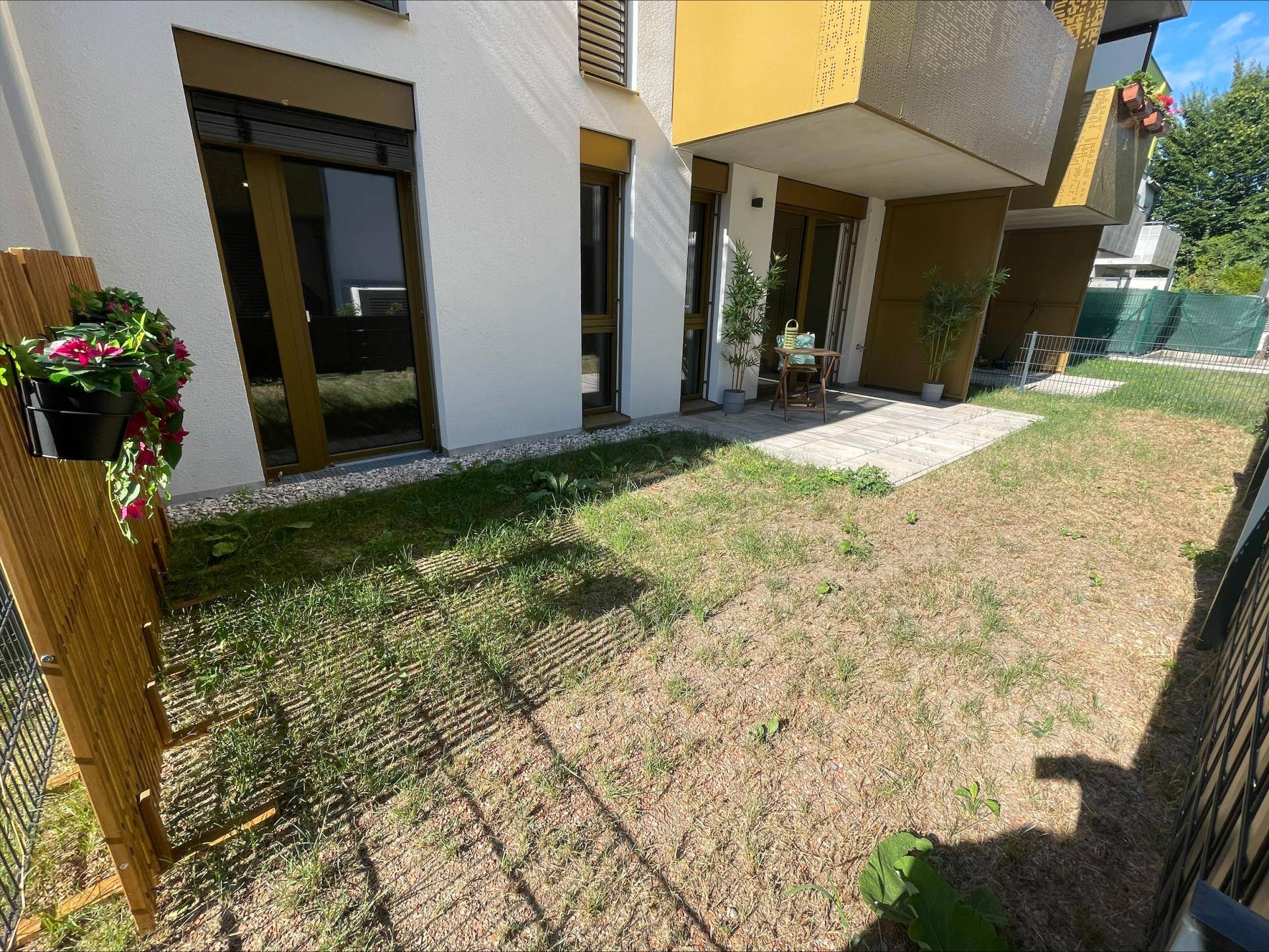 Kleiner privater Gartenbereich mit Rasen und Zugang zur Wohnung, umgeben von einem Zaun.