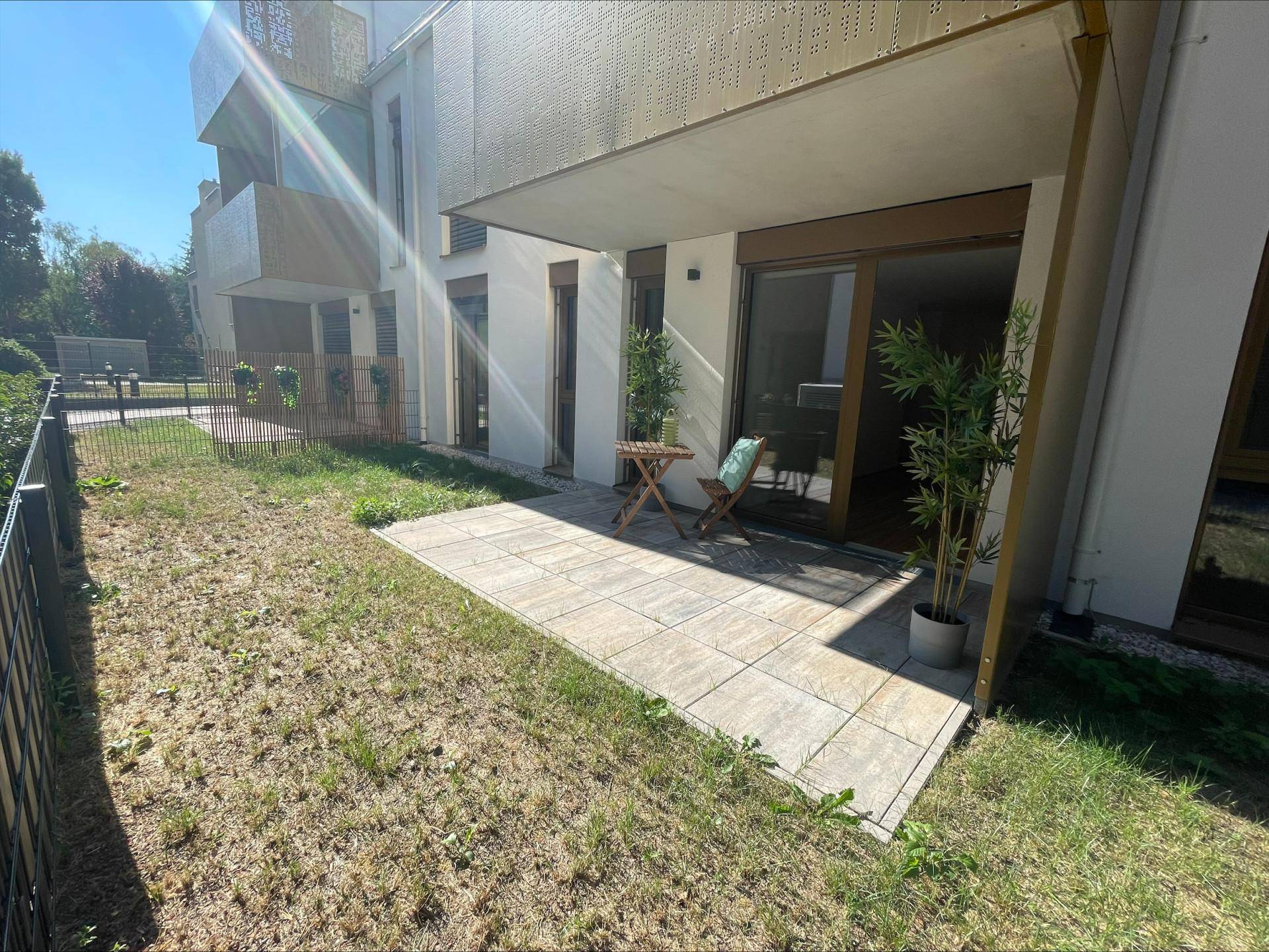 Großzügige Terrasse mit angrenzendem Garten und Blick auf die moderne Gebäudefassade.
