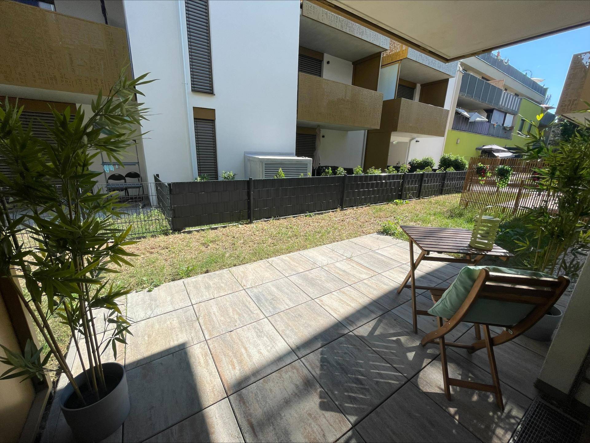 Sonniger Terrassenbereich mit Fliesenboden und kleinem Garten, umgeben von moderner Architektur.