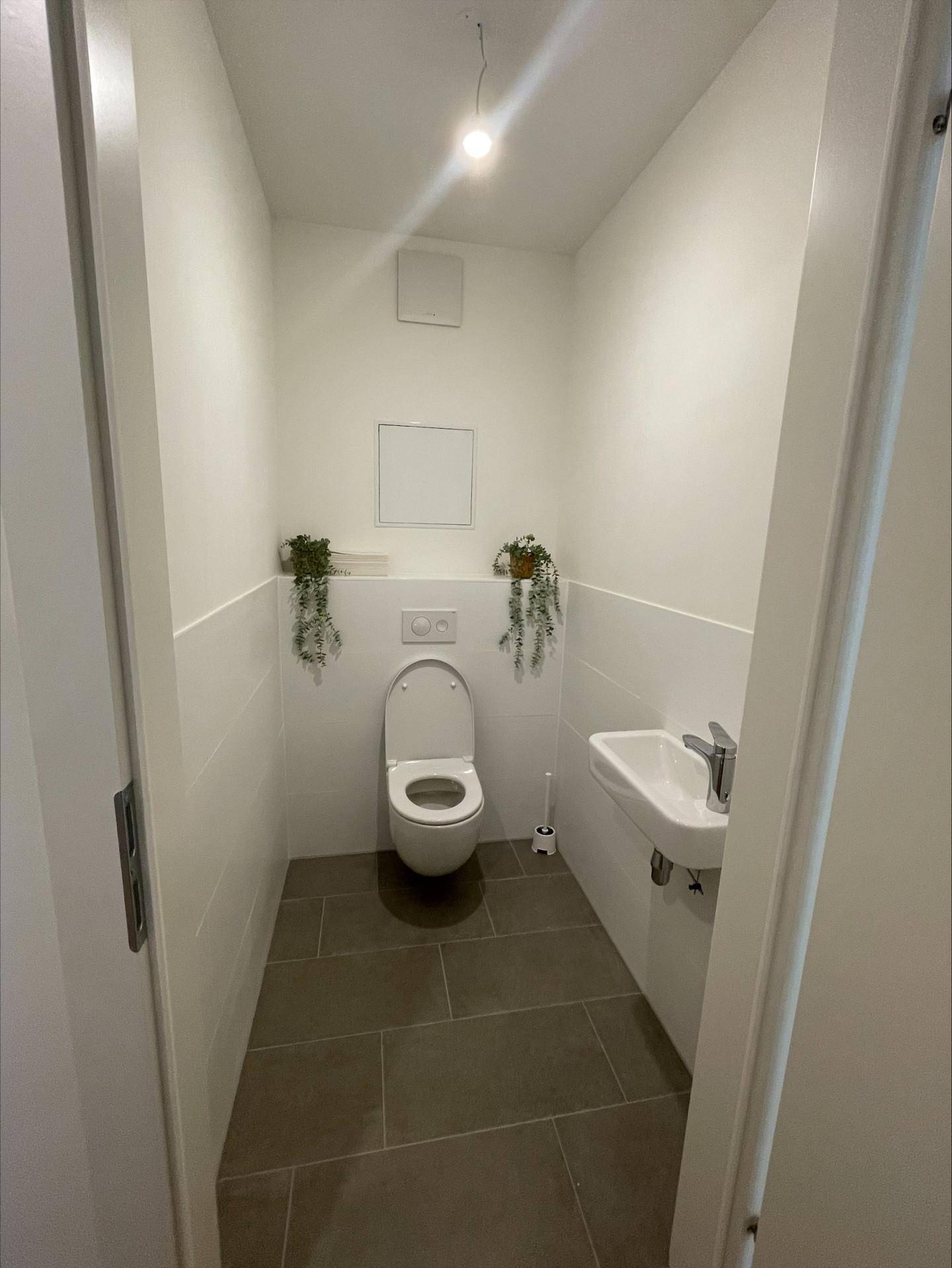 Separates Gäste-WC mit wandhängender Toilette und kleinem Handwaschbecken auf Fliesenboden.