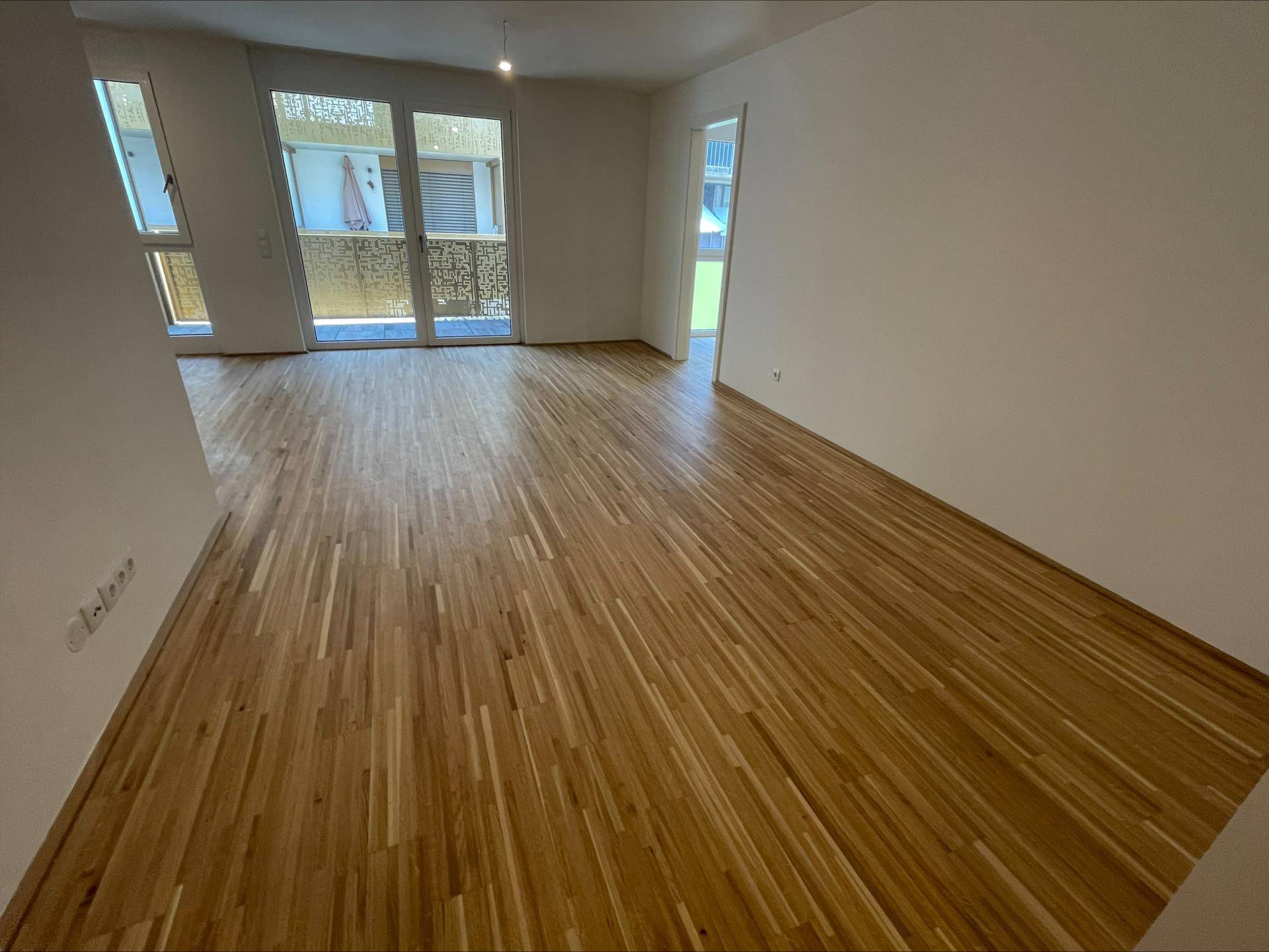 Heller, unmöblierter Wohnbereich mit Holzboden und direktem Zugang zum Balkon.