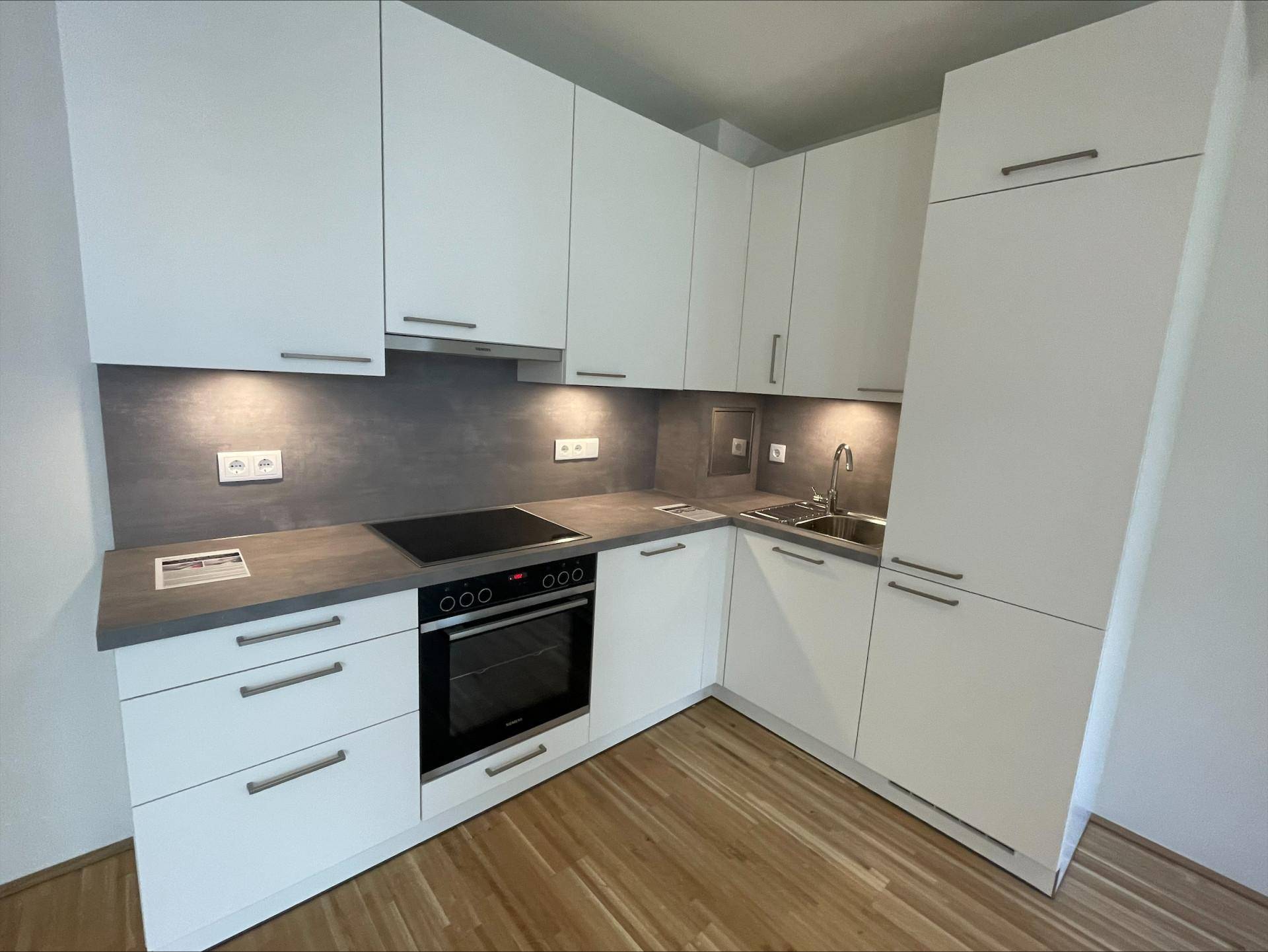 Moderne Einbauküche mit weißen Schränken, dunkler Arbeitsplatte und integrierten Geräten.