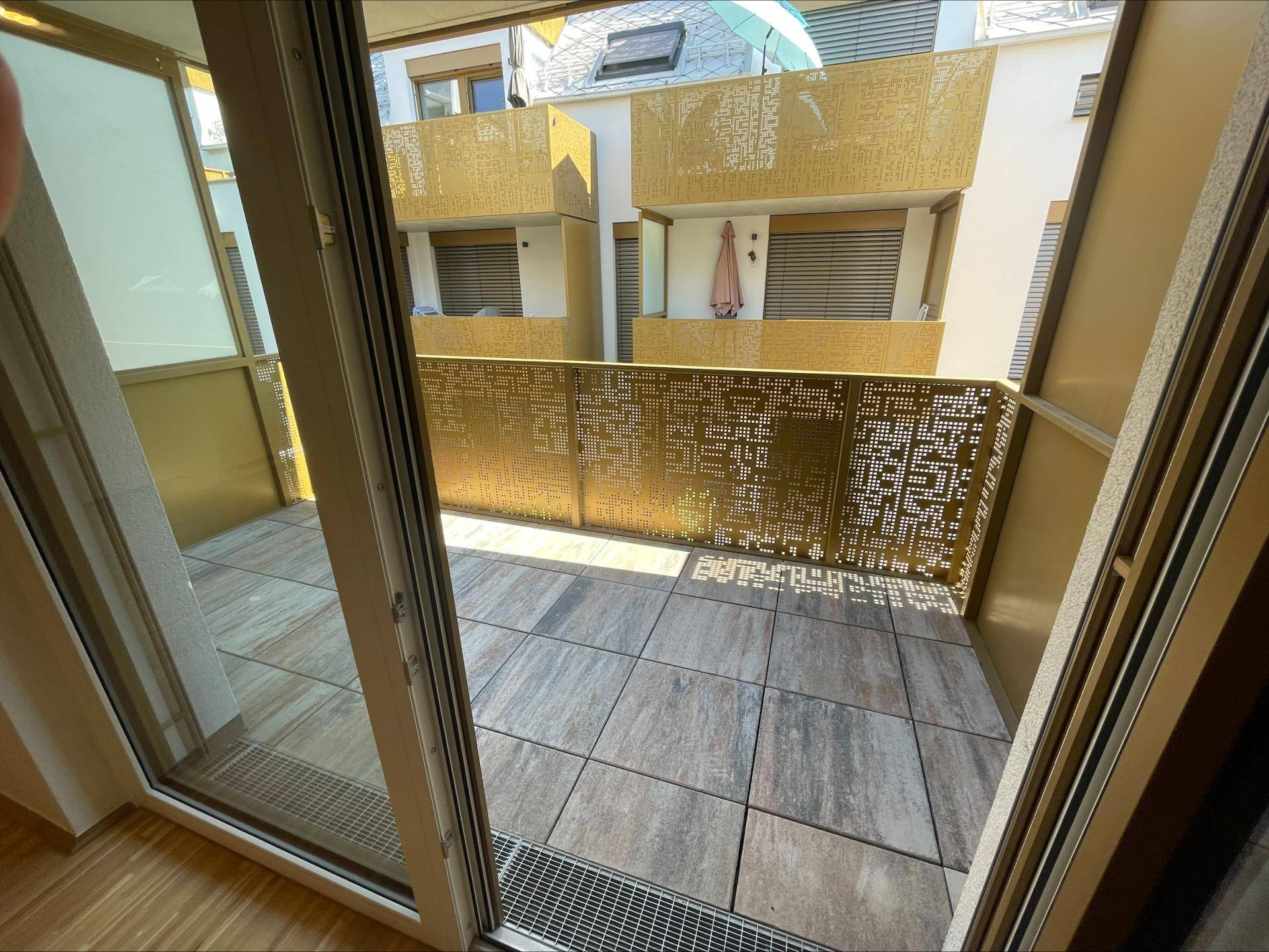 Balkon mit Fliesenboden und moderner Brüstung, gesehen durch eine große Glastür.