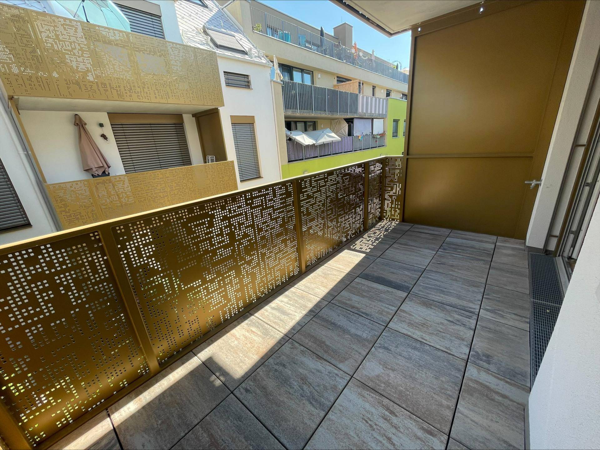 Geräumiger Balkon mit Fliesenboden und moderner, perforierter Metallbrüstung.