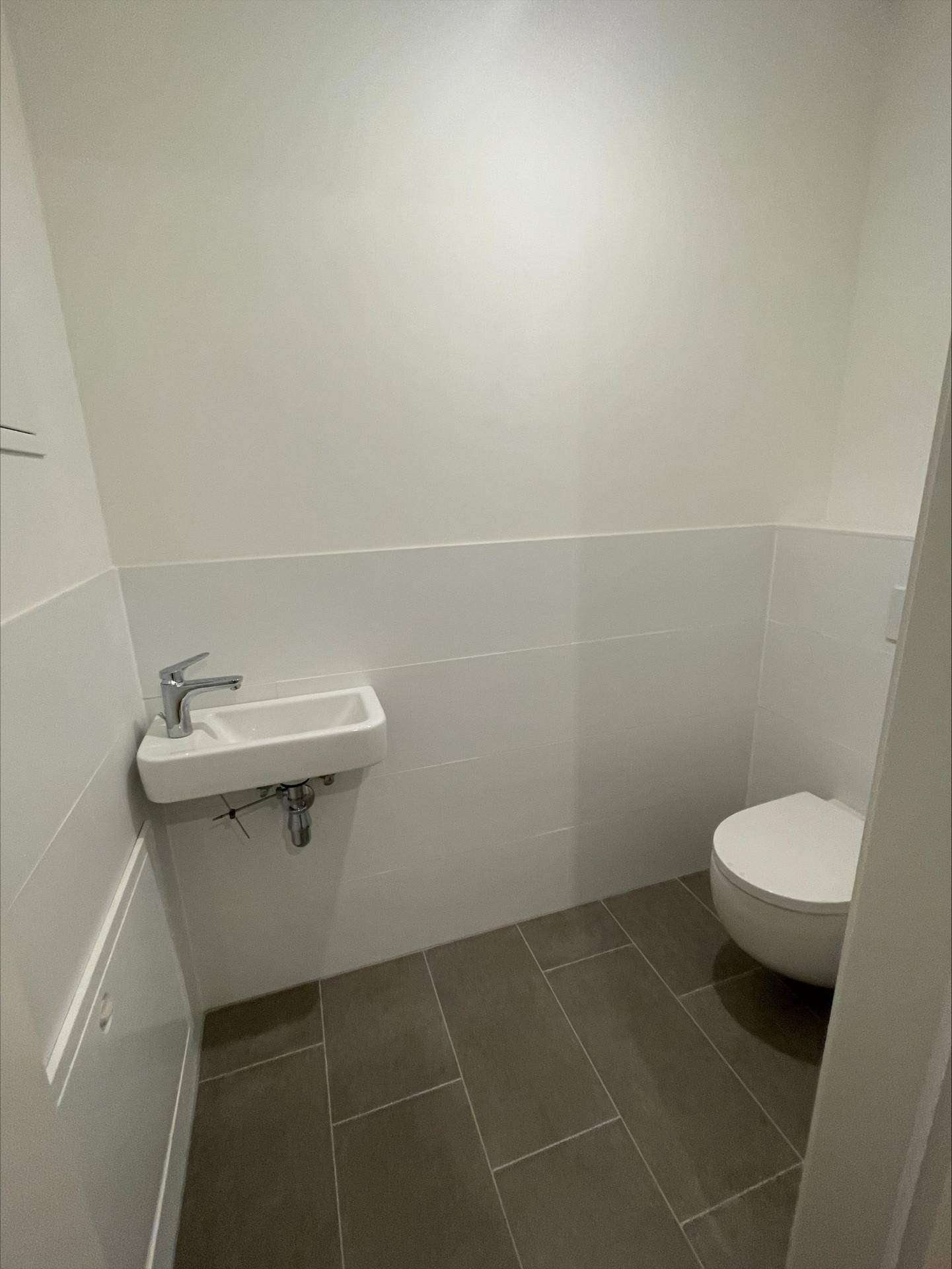 Separates Gäste-WC mit wandhängender Toilette, kleinem Waschbecken und Fliesenboden.