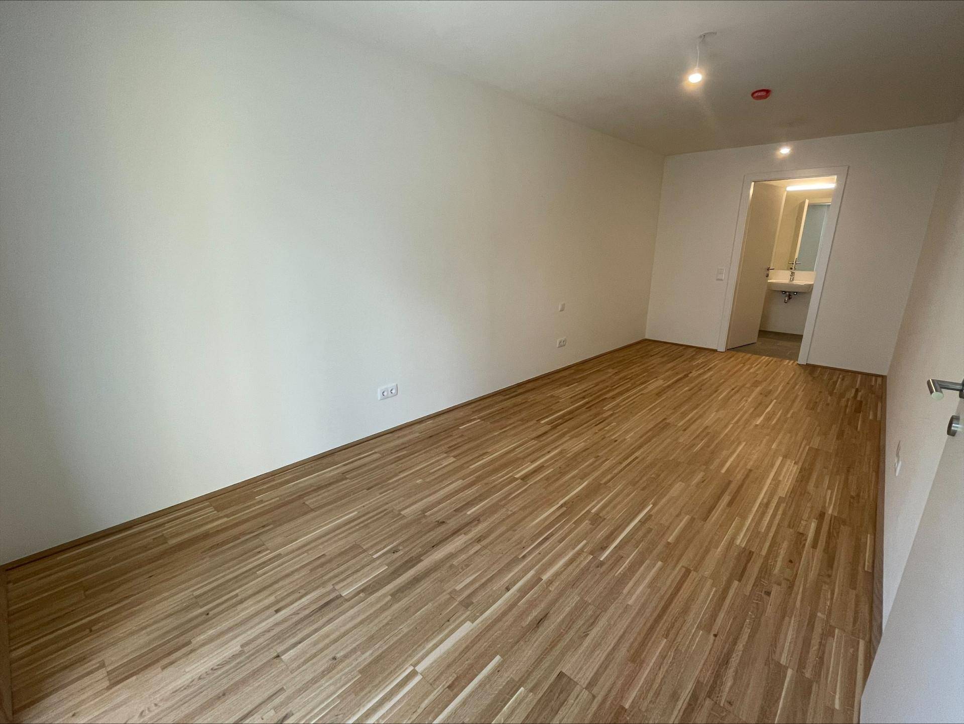 Unmöbliertes Schlafzimmer mit Holzboden und direktem Zugang zu einem Badezimmer.