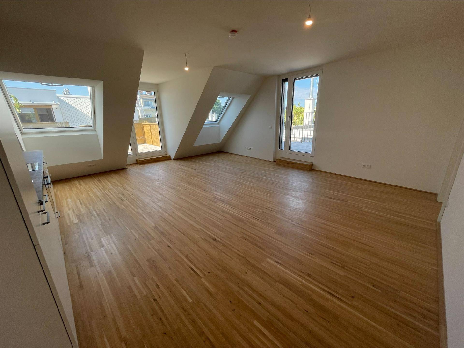 Lichtdurchfluteter Wohnbereich mit Holzboden, großen Fenstern und direktem Zugang zur Außenterrasse.