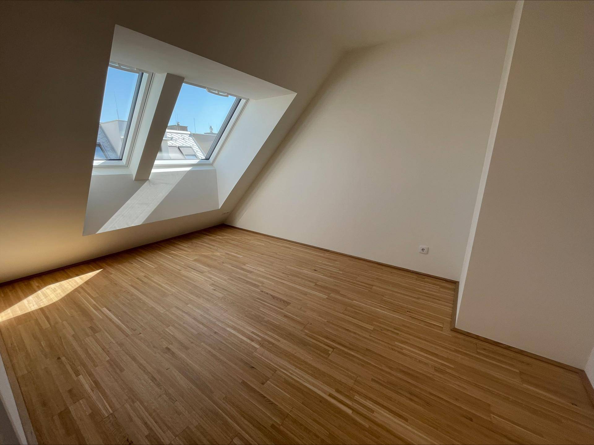 Helles Schlafzimmer mit Holzboden, weißen Wänden und mehreren Dachfenstern unter der Dachschräge.