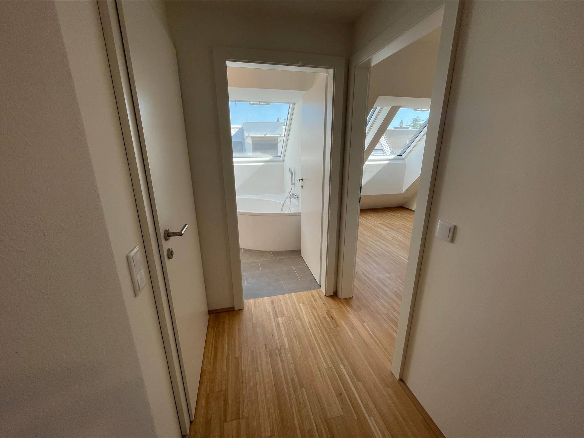 Blick vom Flur in ein Badezimmer mit Badewanne und einen weiteren Raum, beide mit Dachfenstern.