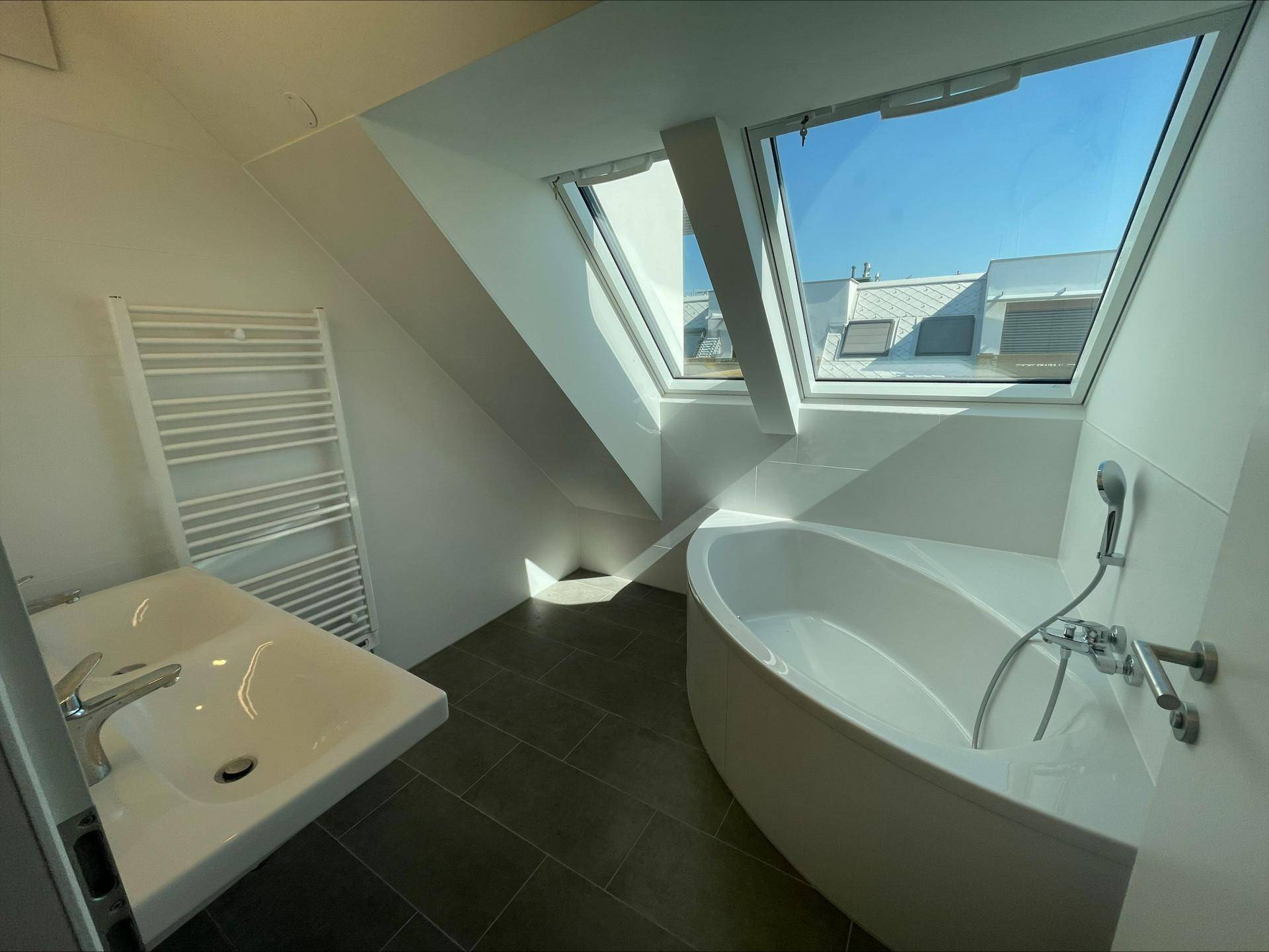 Modernes Badezimmer mit Eckbadewanne, Einzelwaschbecken, Handtuchheizkörper und großen Dachfenstern.