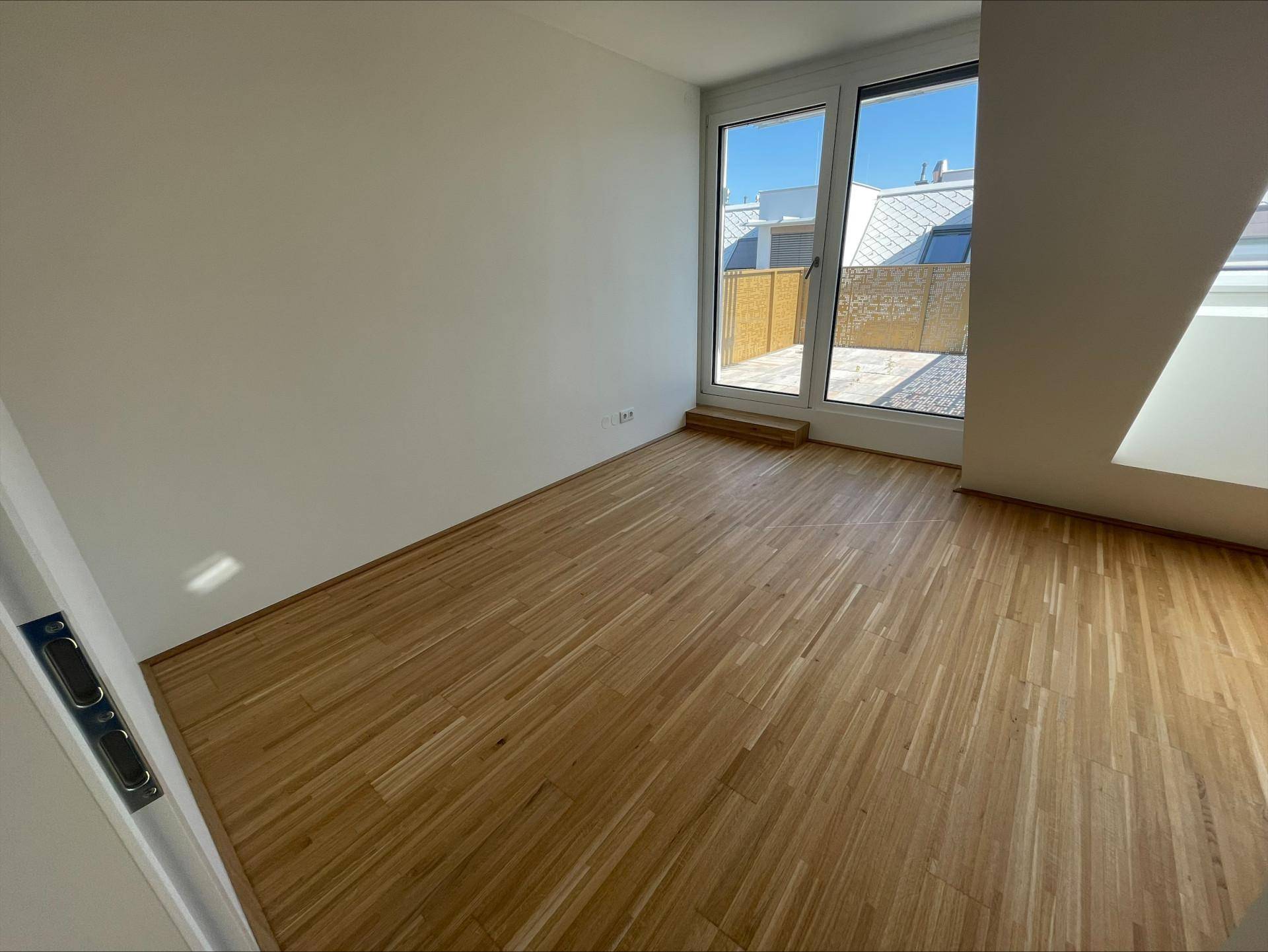 Helles Zimmer mit Holzboden und Zugang zur Terrasse durch eine große Glastür, bietet viel Tageslicht.