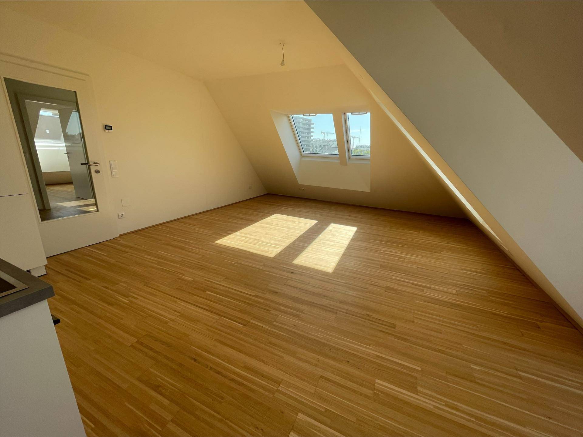 Geräumiger Wohnbereich mit hellem Holzboden und großen Dachfenstern, die viel Sonnenlicht hereinlassen.
