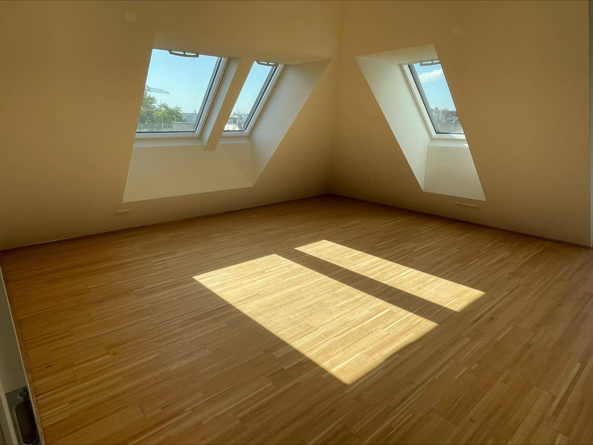 Lichtdurchfluteter Wohnraum mit Holzboden und mehreren Dachfenstern, die eine helle Atmosphäre schaffen.
