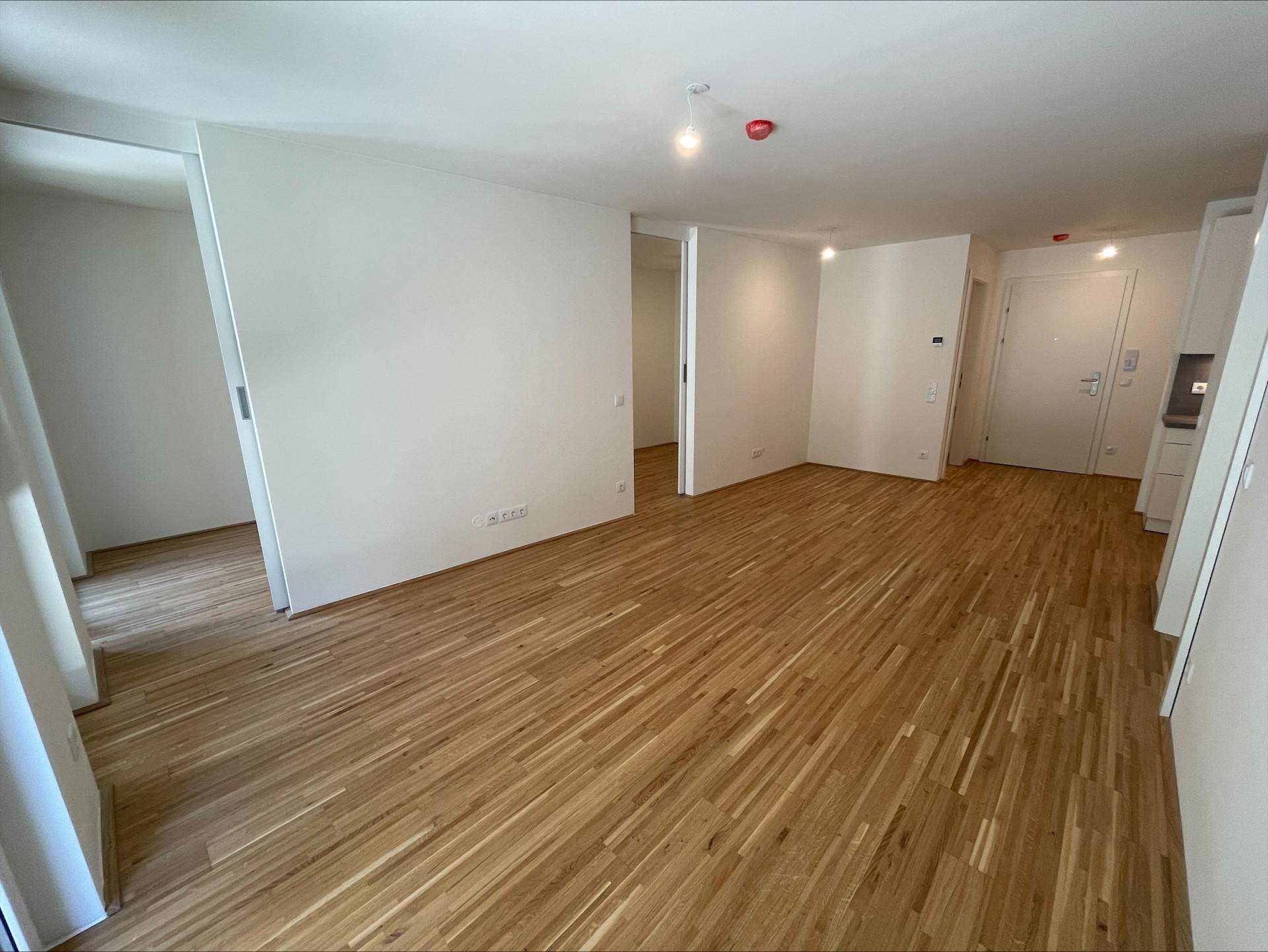 Geräumiger, leerer Wohnbereich mit Holzboden und weißen Wänden, der vielseitige Gestaltungsmöglichkeiten bietet.