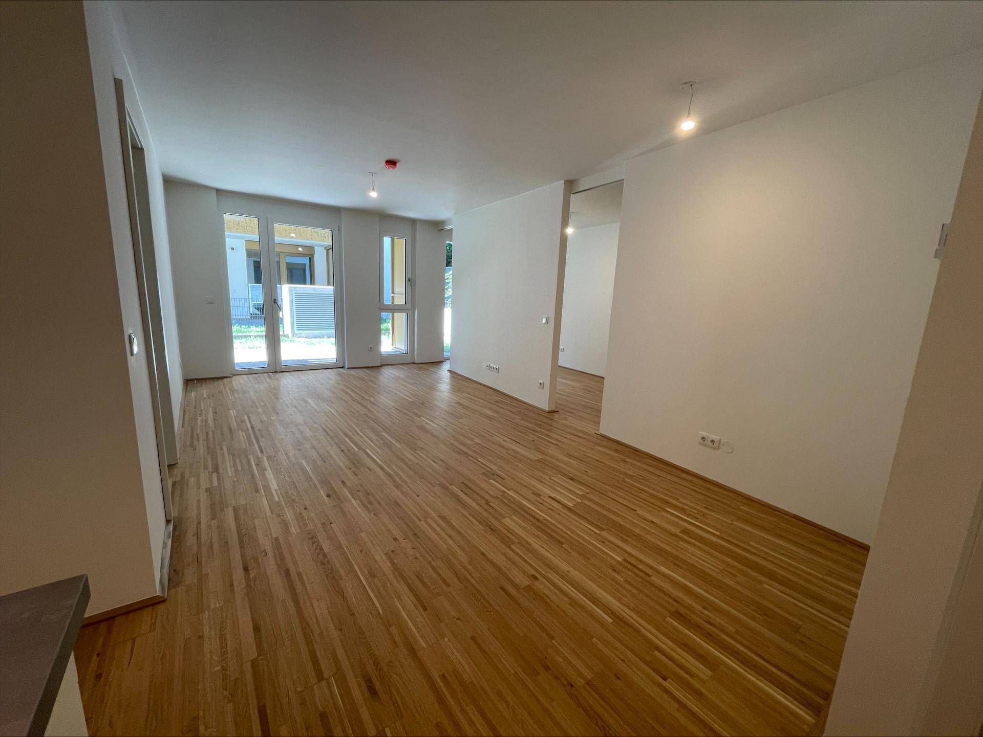 Heller Wohnbereich mit Holzboden und großen Fenstern, die Zugang zu einem Außenbereich ermöglichen.